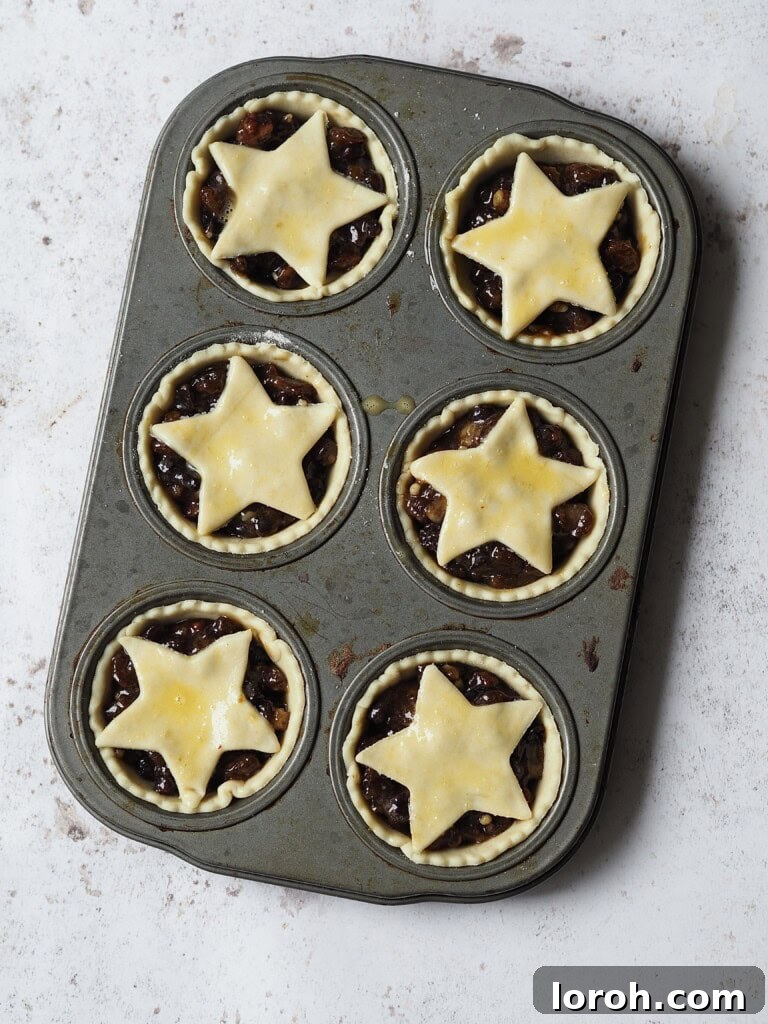 Tray of uncooked mince pies with mincemeat filling and pastry stars on top.