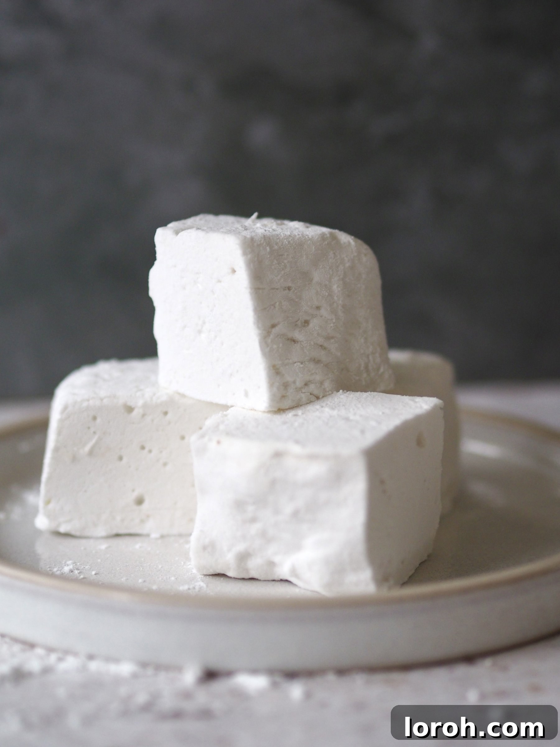 A beautiful stack of fluffy homemade marshmallows on a plate, perfectly dusted and ready to be enjoyed.