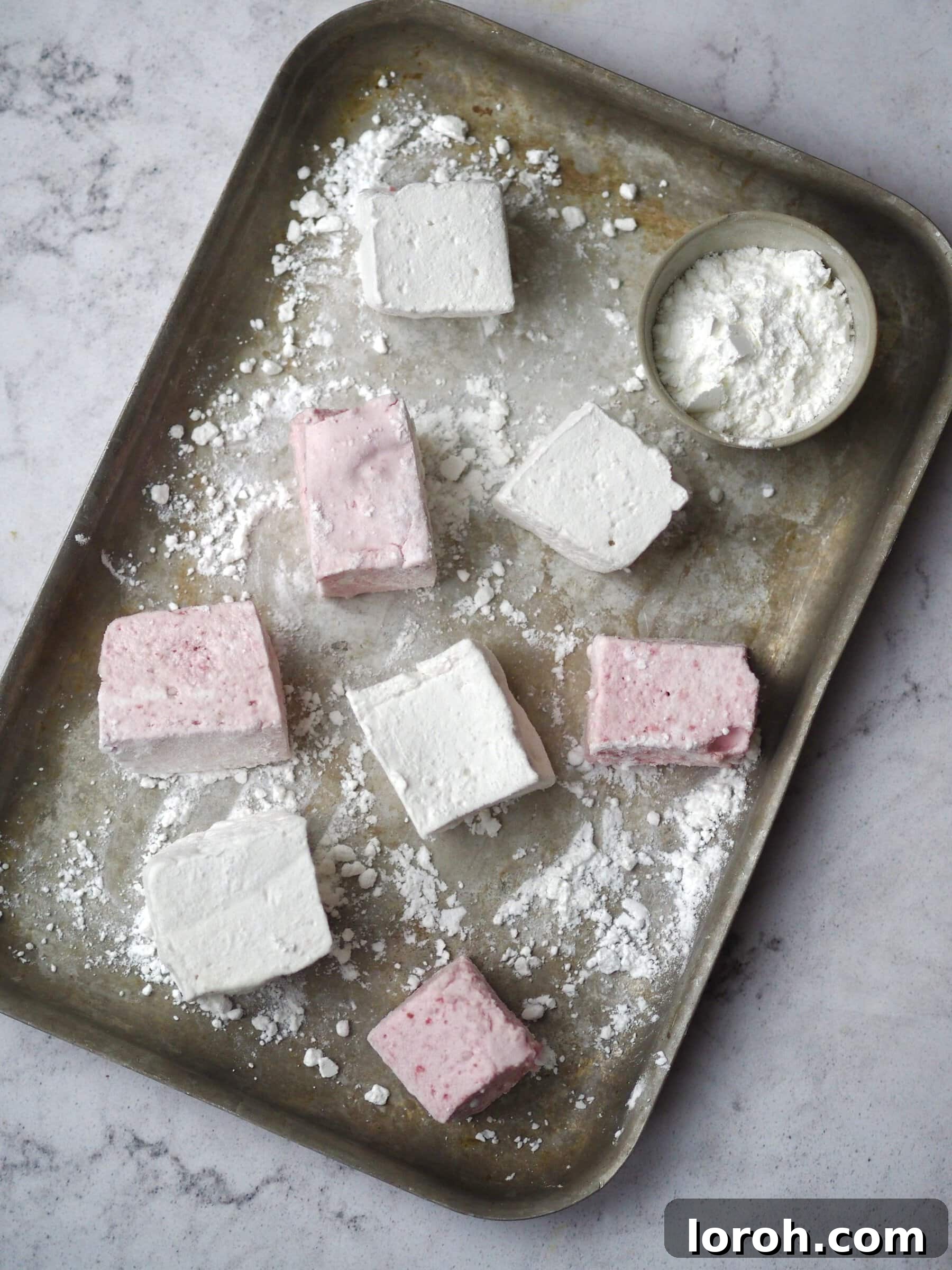 Freshly cut homemade marshmallows liberally dusted with icing sugar and cornflour on a baking tray.