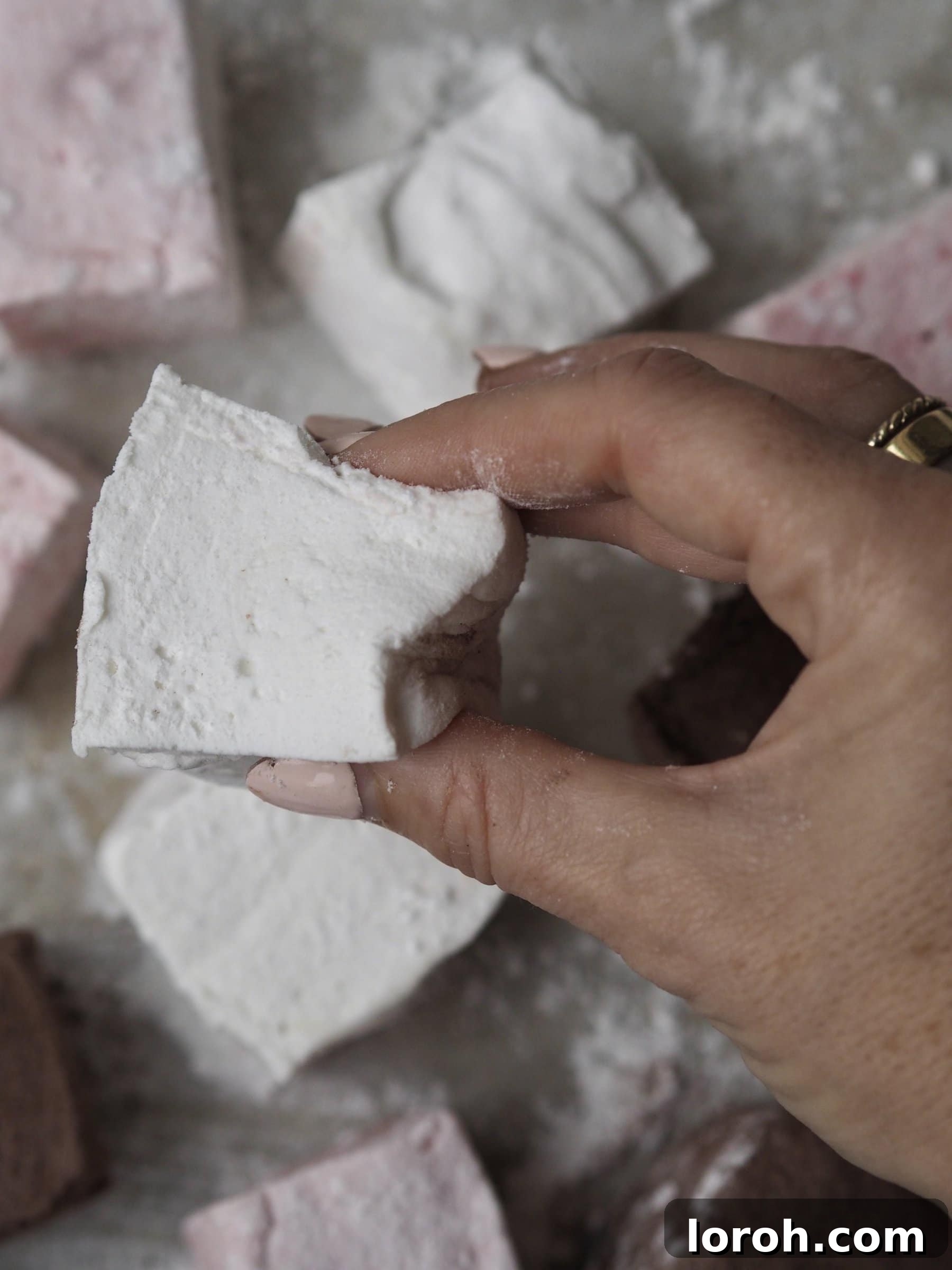 A single homemade marshmallow being gently squeezed, visually demonstrating its perfect soft and springy texture.