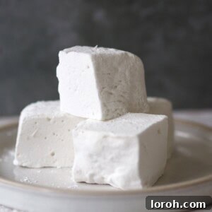A stack of perfectly crafted homemade marshmallows on a plate, beautifully dusted and ready to be served.
