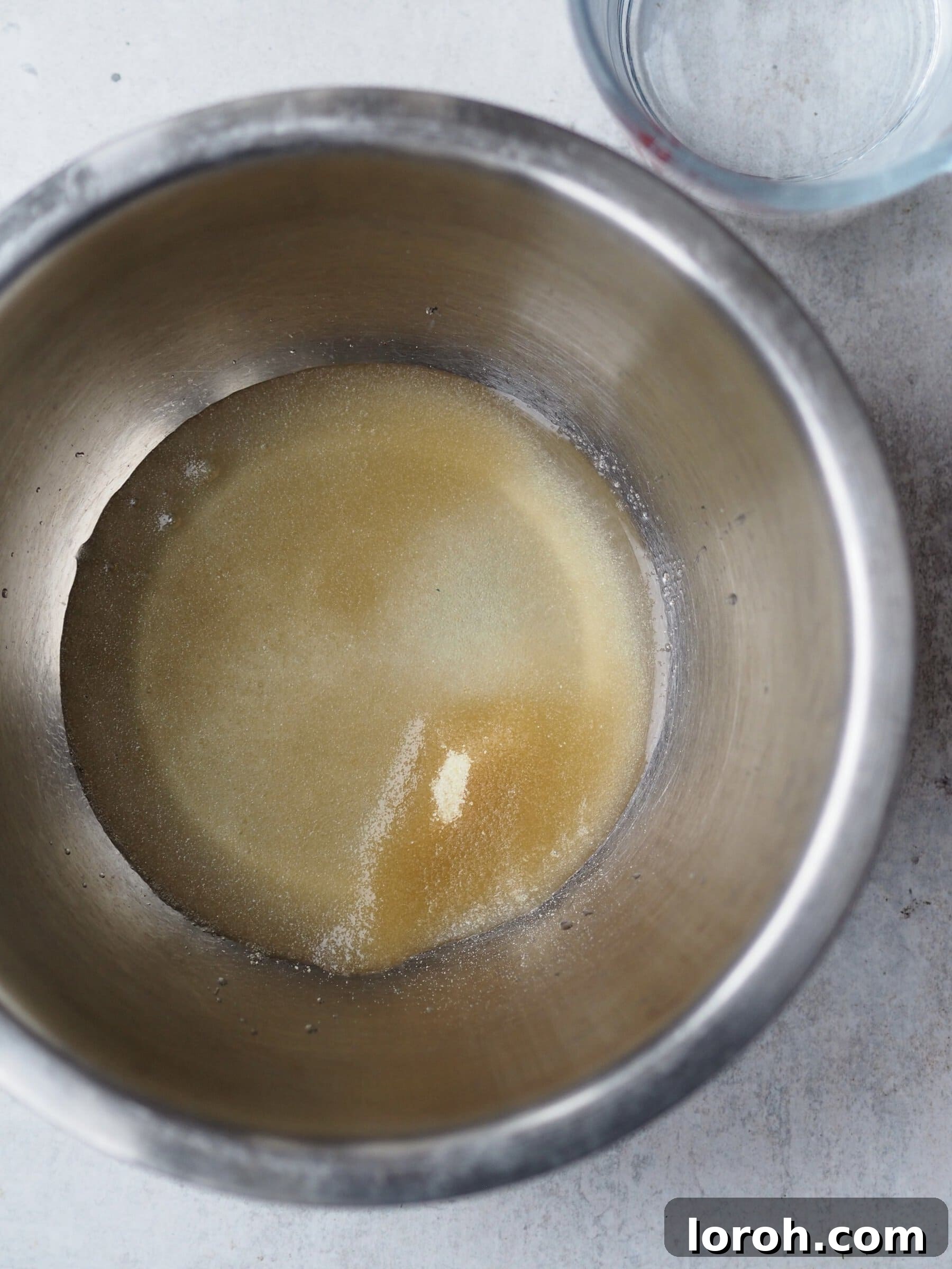 Adding gelatine powder to cold water in a bowl to begin the blooming process.