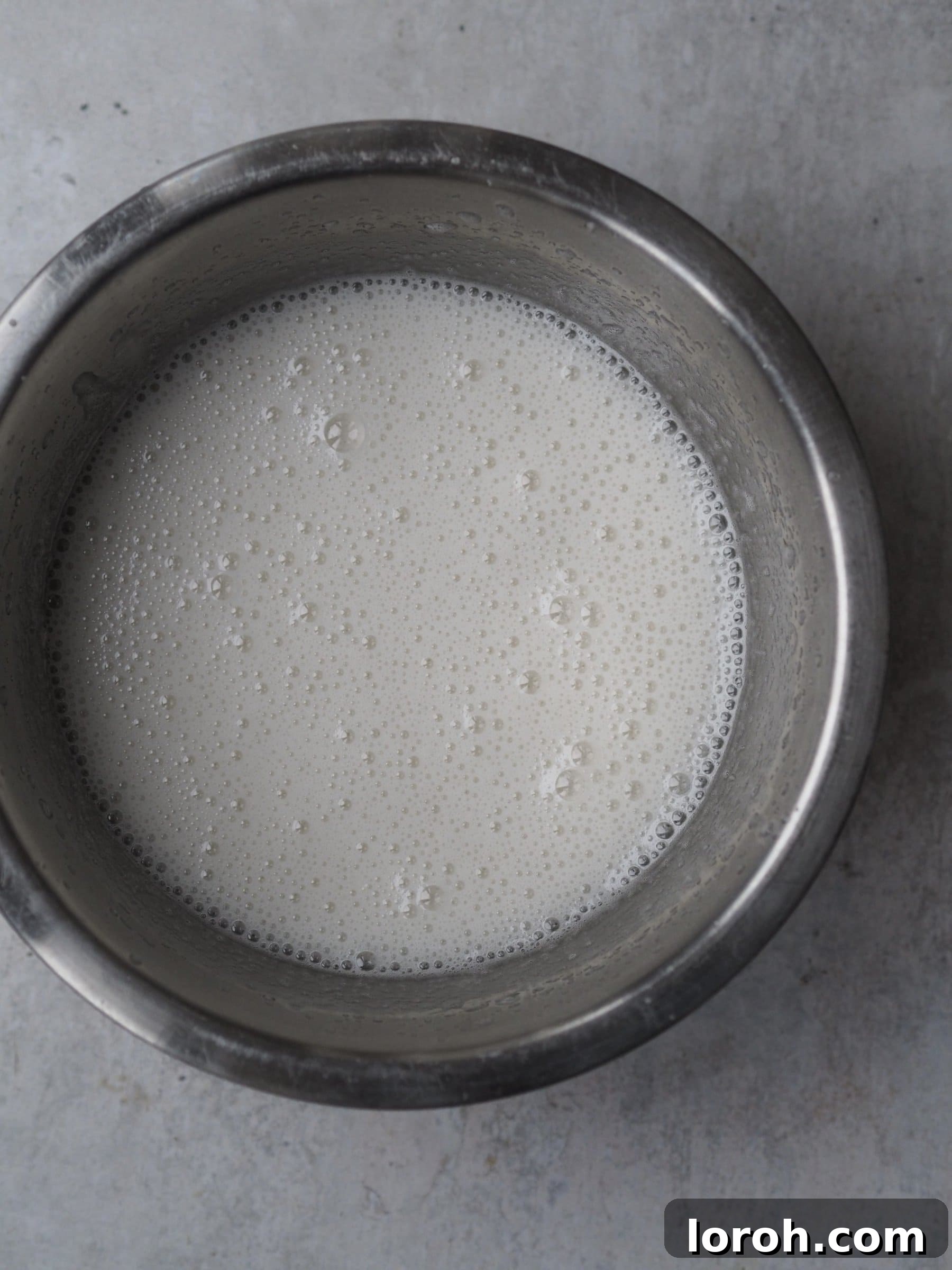 Carefully drizzling hot sugar syrup into the bloomed gelatine mixture while continuously whisking.