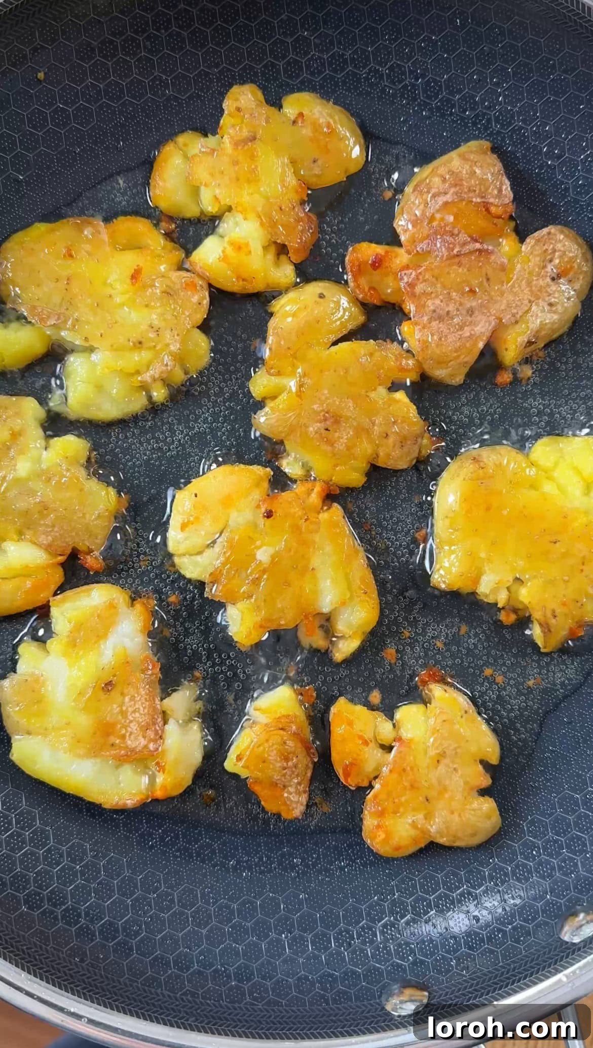 Smashed potatoes shallow frying in a large non-stick pan until golden brown and crispy.