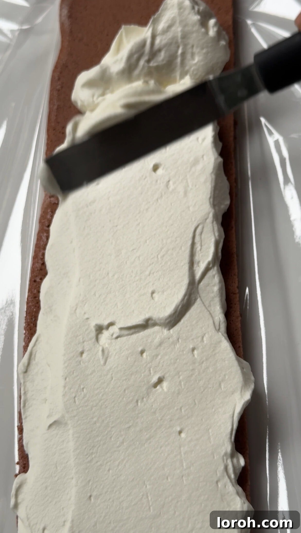 Winter Woodland Roll 13 spreading whipped cream on the yule log cake.