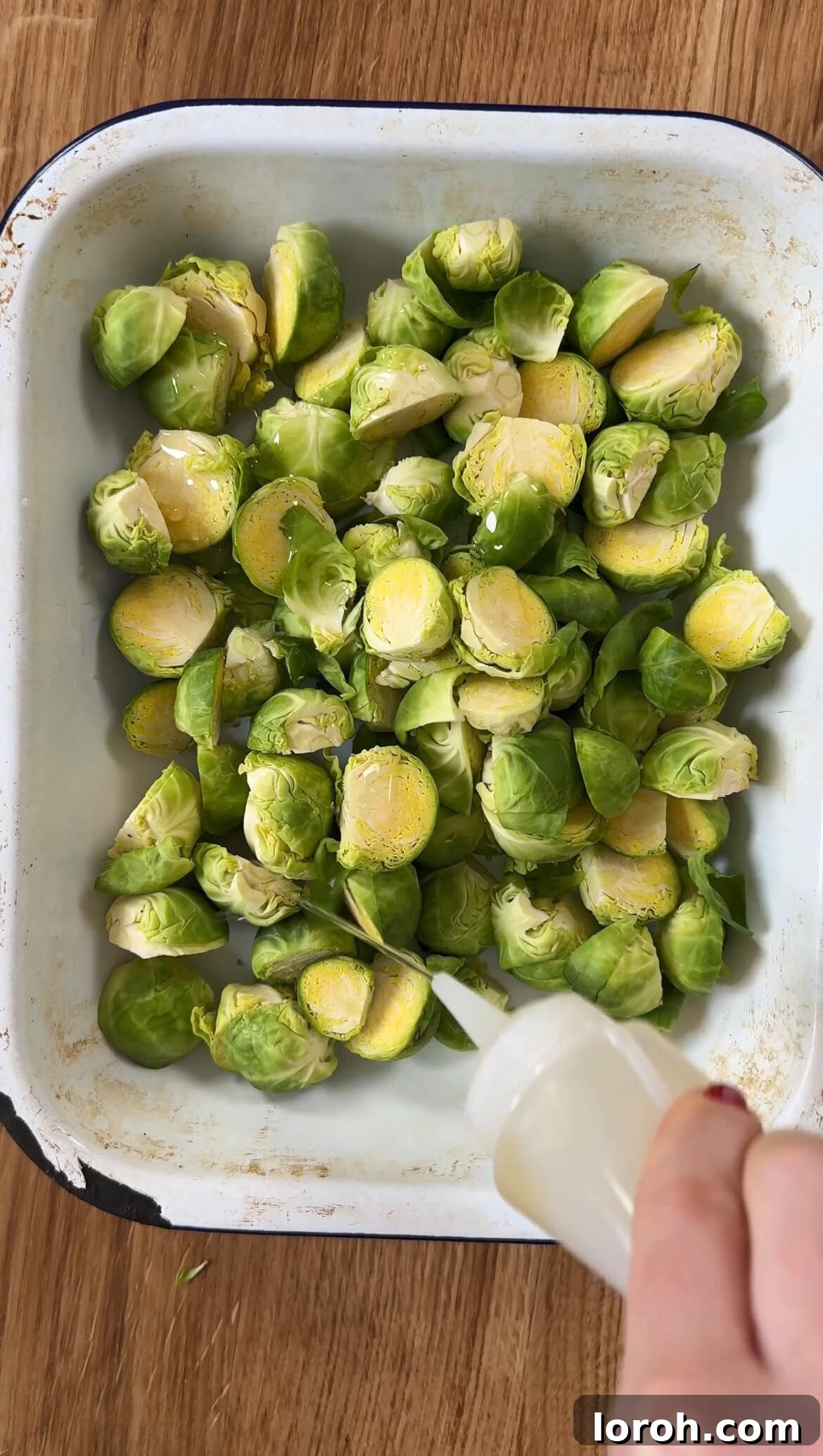 Brussels sprouts being roasted in a tin with olive oil, salt, and pepper, showcasing their preparation for the gratin.
