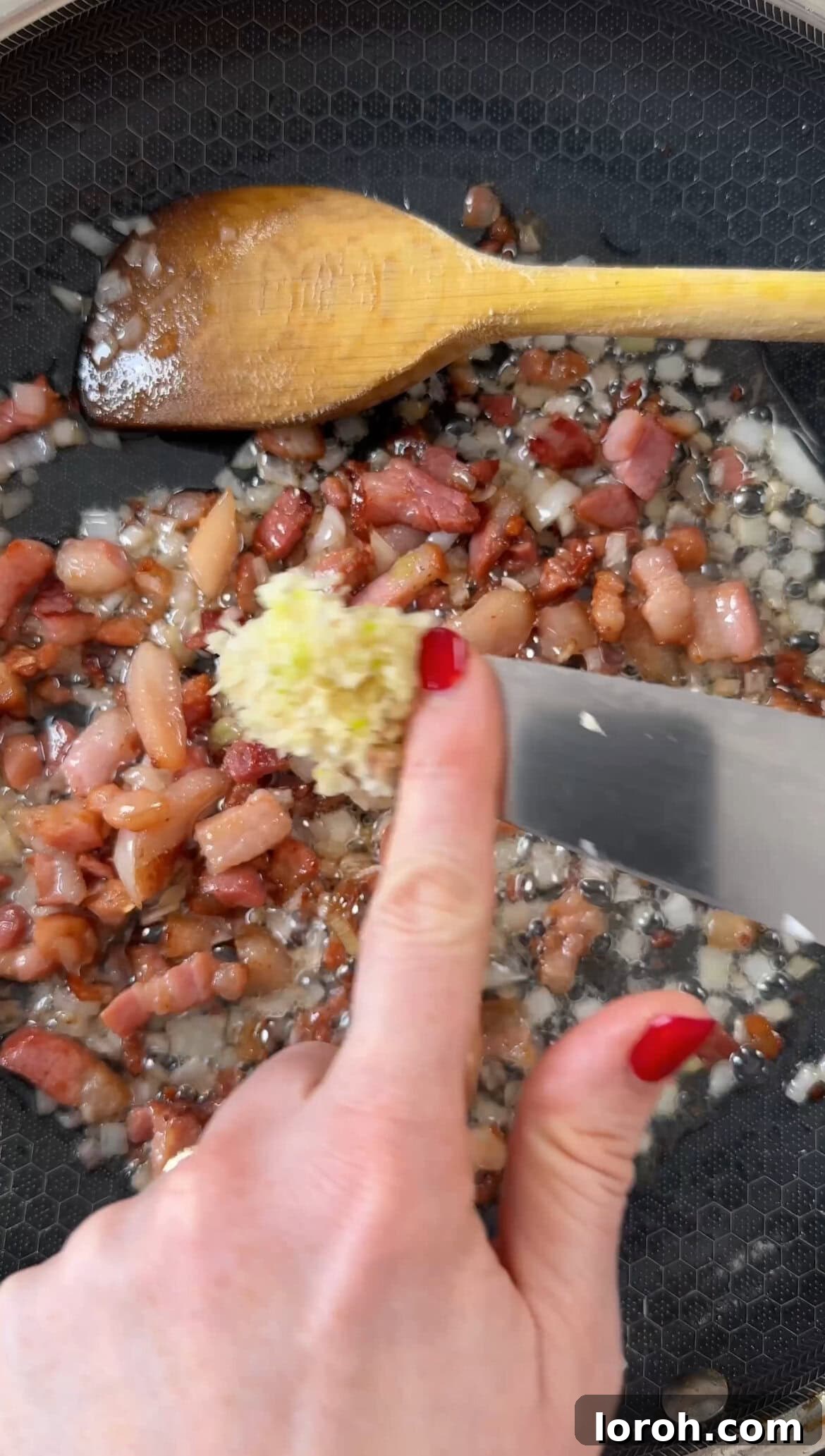 Finely chopped shallots and crushed garlic being added to the rendered pancetta fat in a frying pan, releasing their aromas.