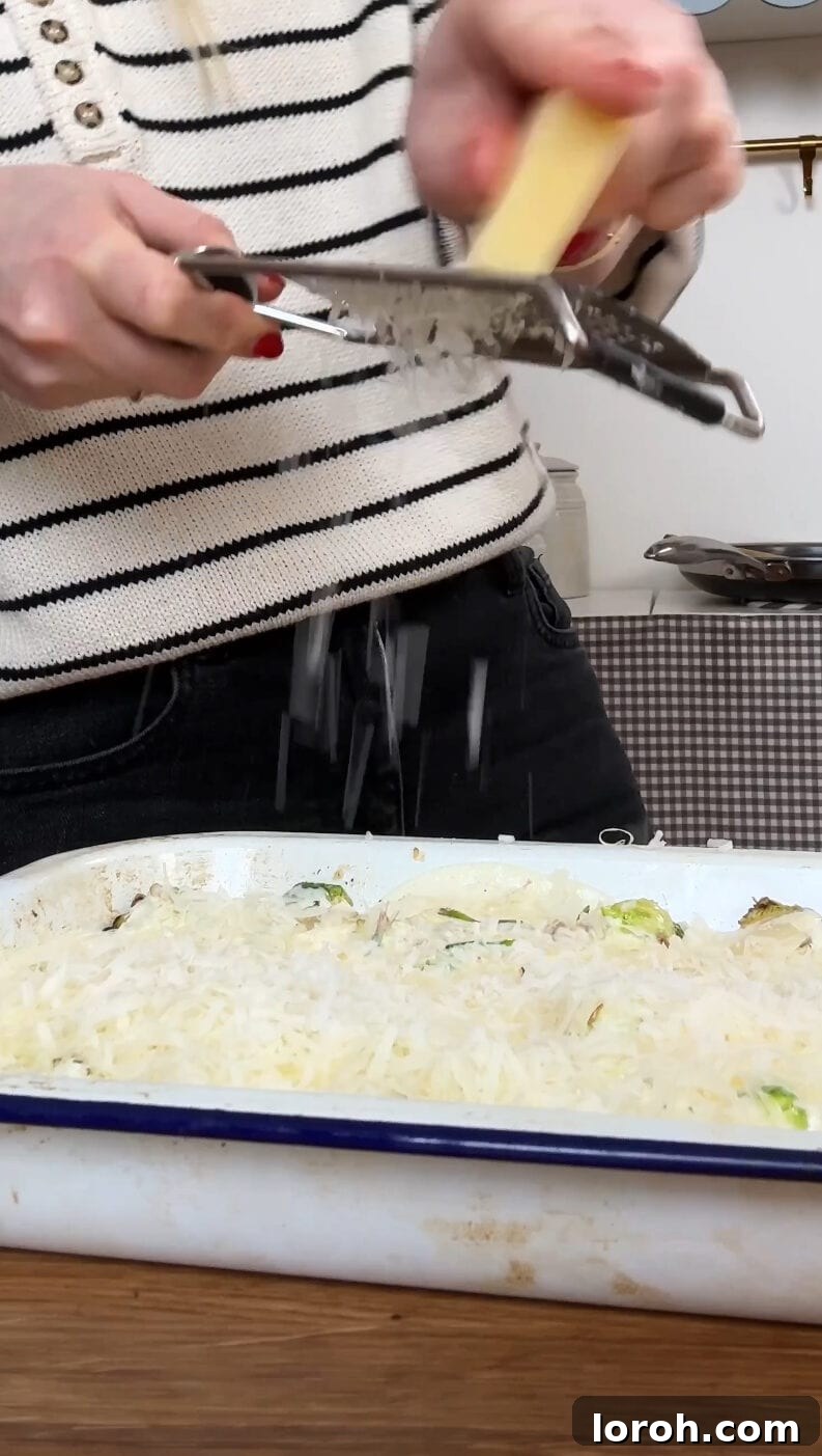 Grating the remaining Gruyere cheese over the creamy Brussels sprouts with pancetta before the final baking step, for a golden crust.