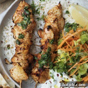 Appetizing image of baked chicken skewers with herb drizzle, crunchy salad, and raita.
