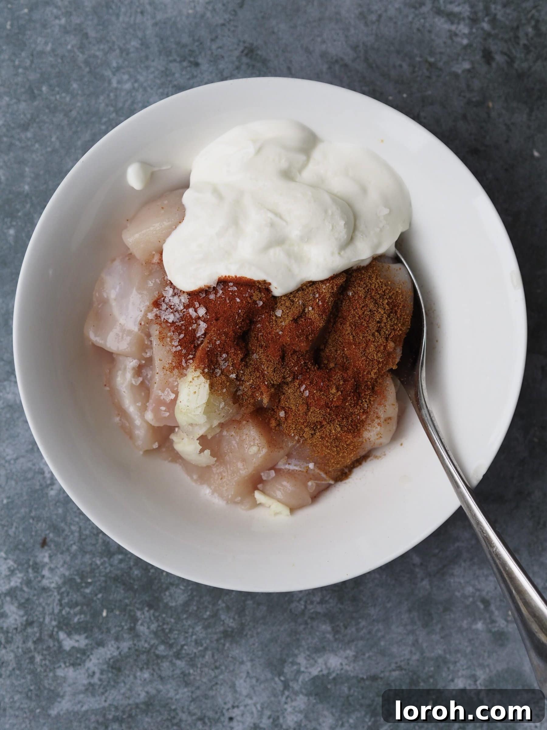 Diced chicken pieces marinating in a bowl with yogurt and spices.