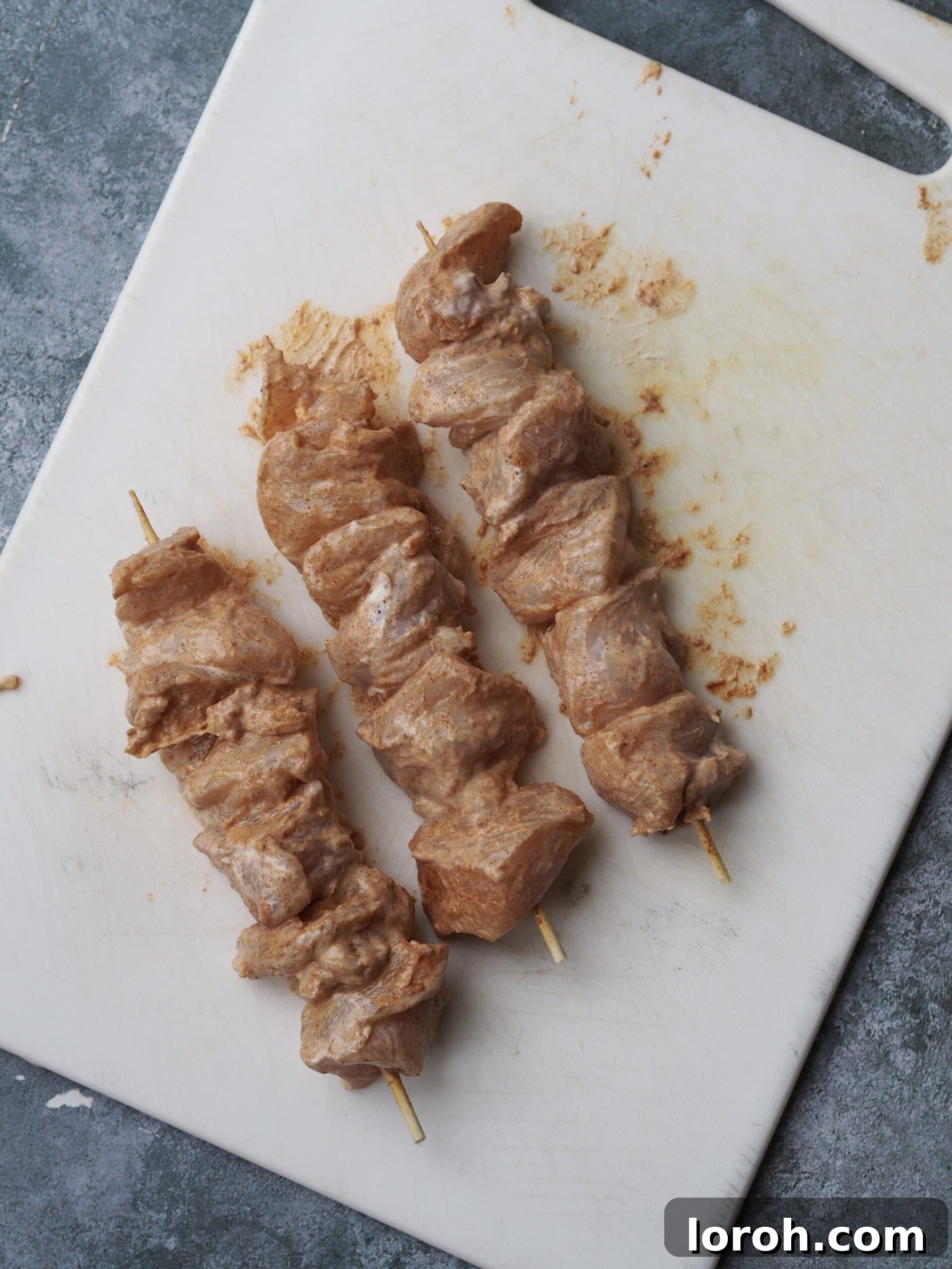 Chicken pieces being threaded onto metal skewers.