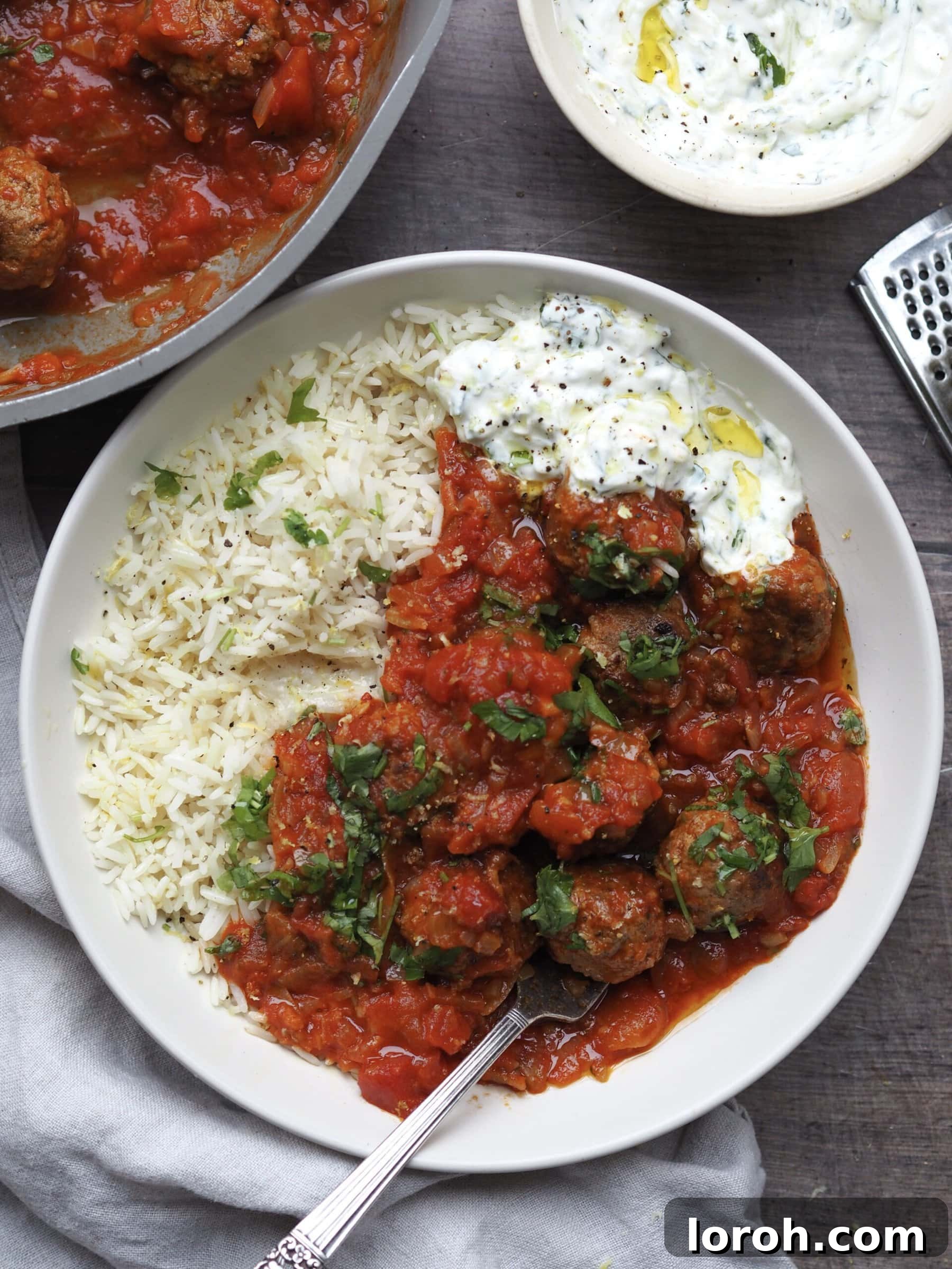 The finished lamb mince meatballs dish, plated with rice, tomato sauce, and a generous dollop of tzatziki.