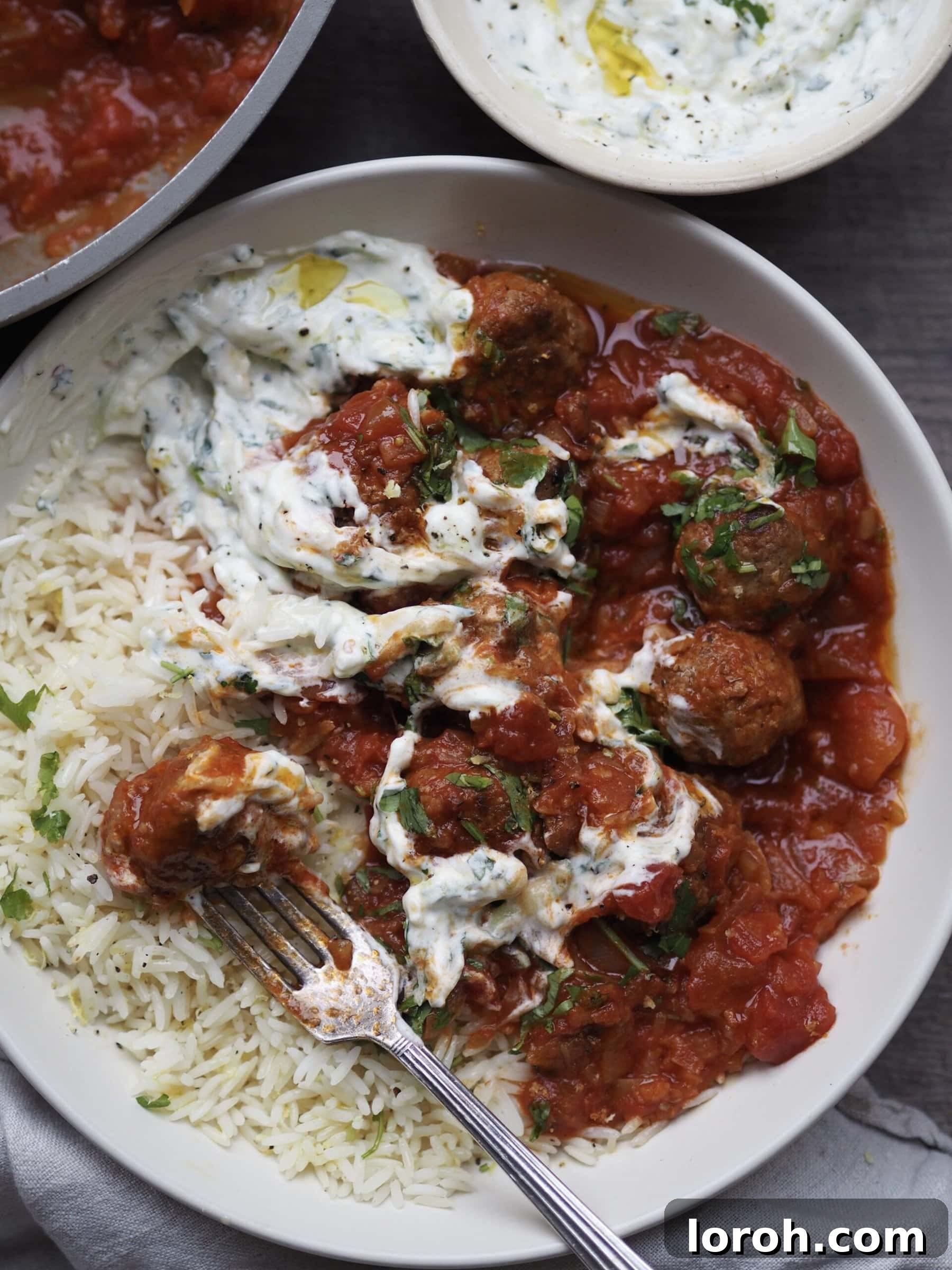 A close-up of golden-brown lamb meatballs simmering in a rich, vibrant tomato sauce, ready to be served.