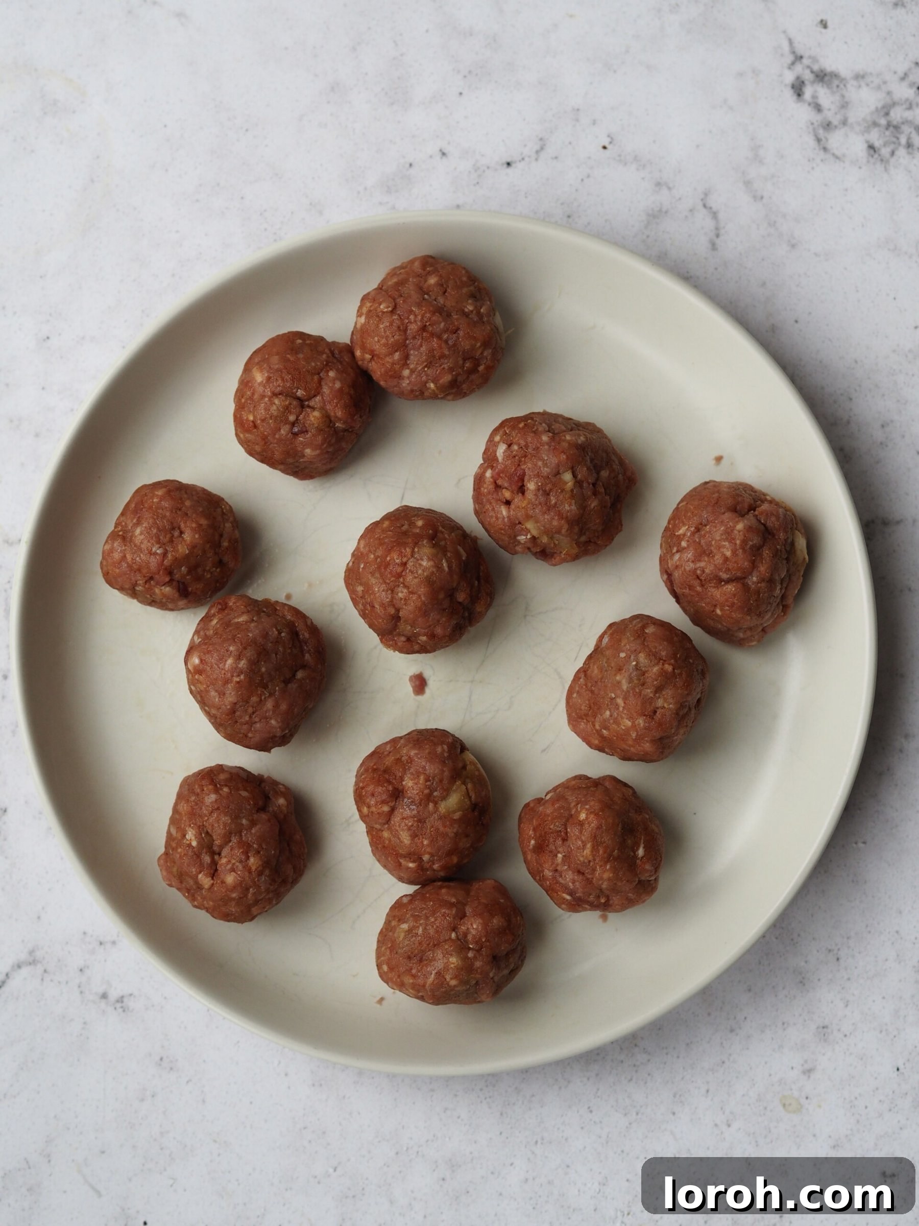 Hands shaping lamb mince into small, uniform meatballs.