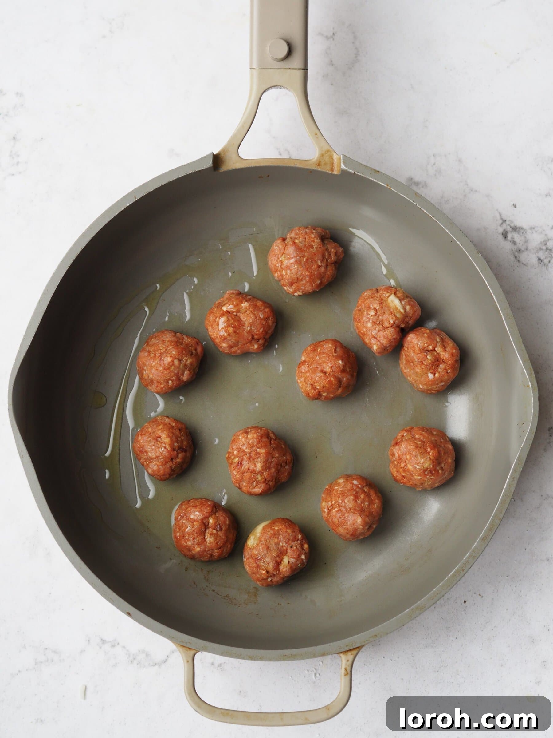 A pan with lamb meatballs sizzling and browning in olive oil.