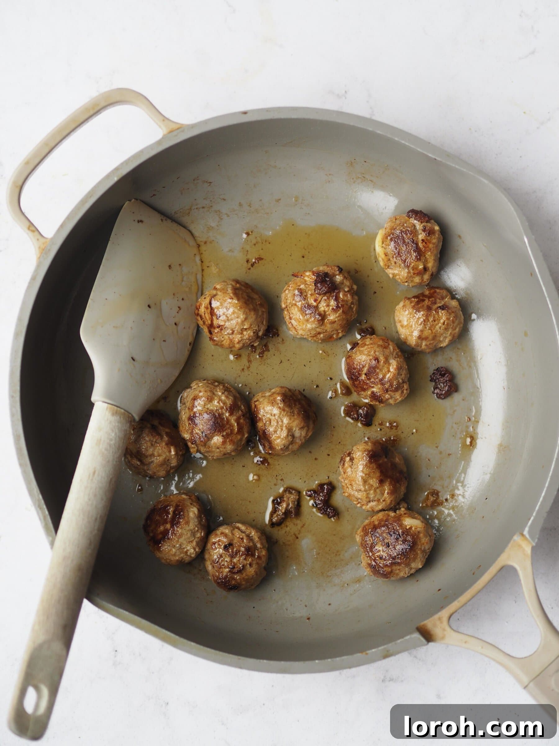 Frying lamb meatballs in a pan, turning them to ensure even browning.