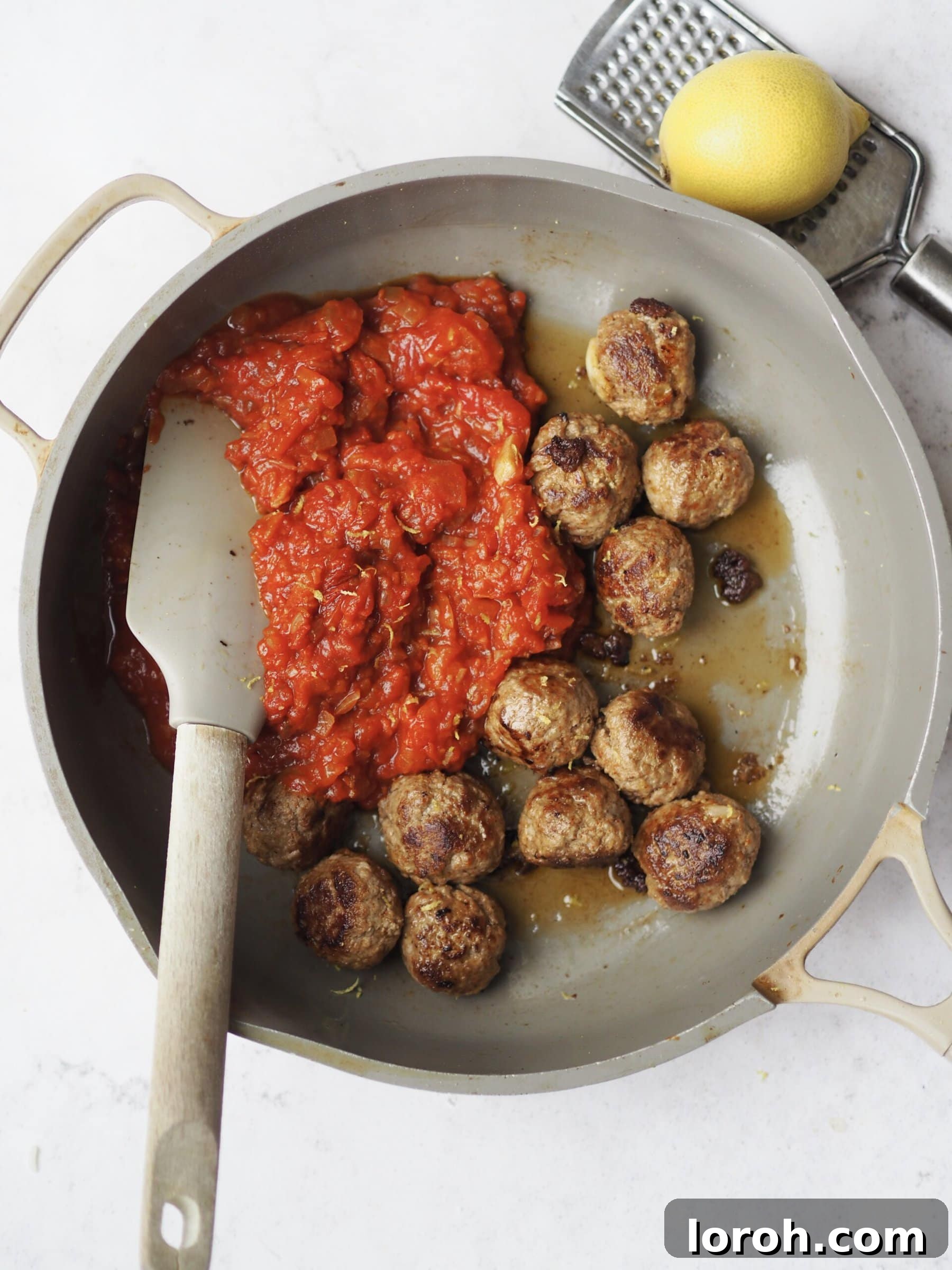 Cooked lamb meatballs being added to the simmering tomato sauce.