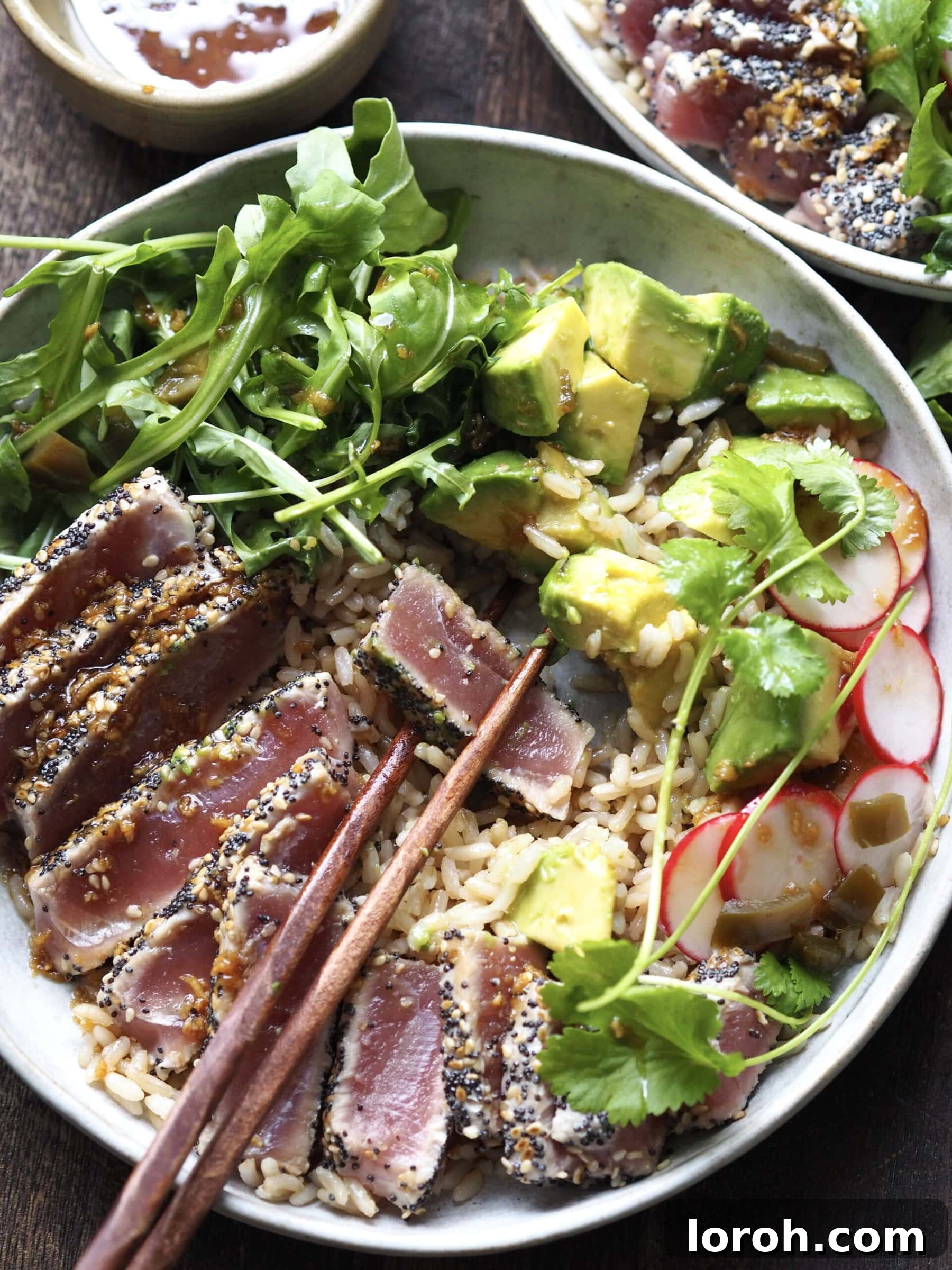 Ahi tuna salad presented with chopsticks poised to pick up a slice of seared tuna, highlighting the beautiful pink center.