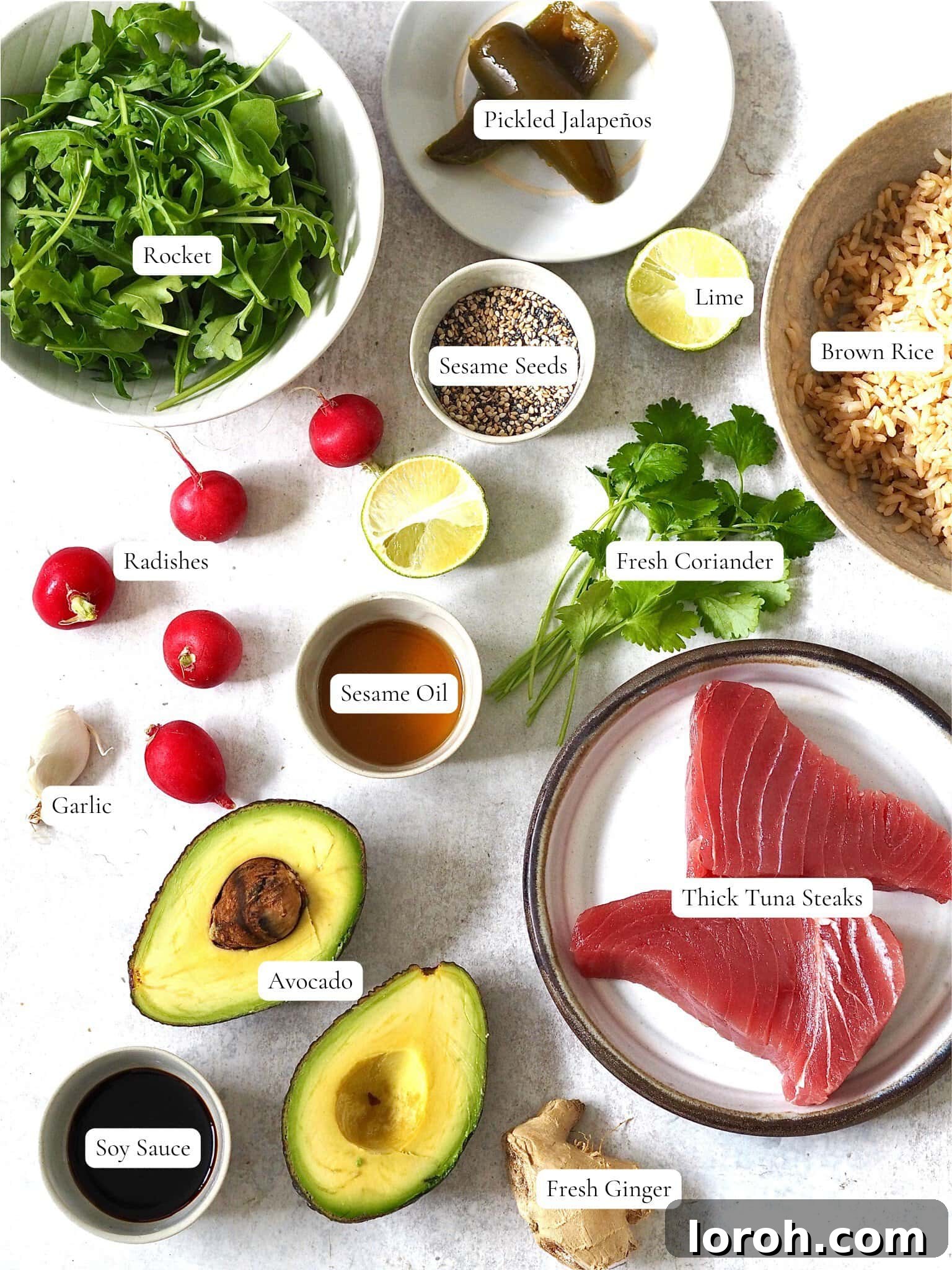 A collection of fresh ingredients laid out on a wooden board, including tuna steaks, lime, ginger, garlic, sesame seeds, avocado, and radishes, ready for the Ahi Tuna Salad.