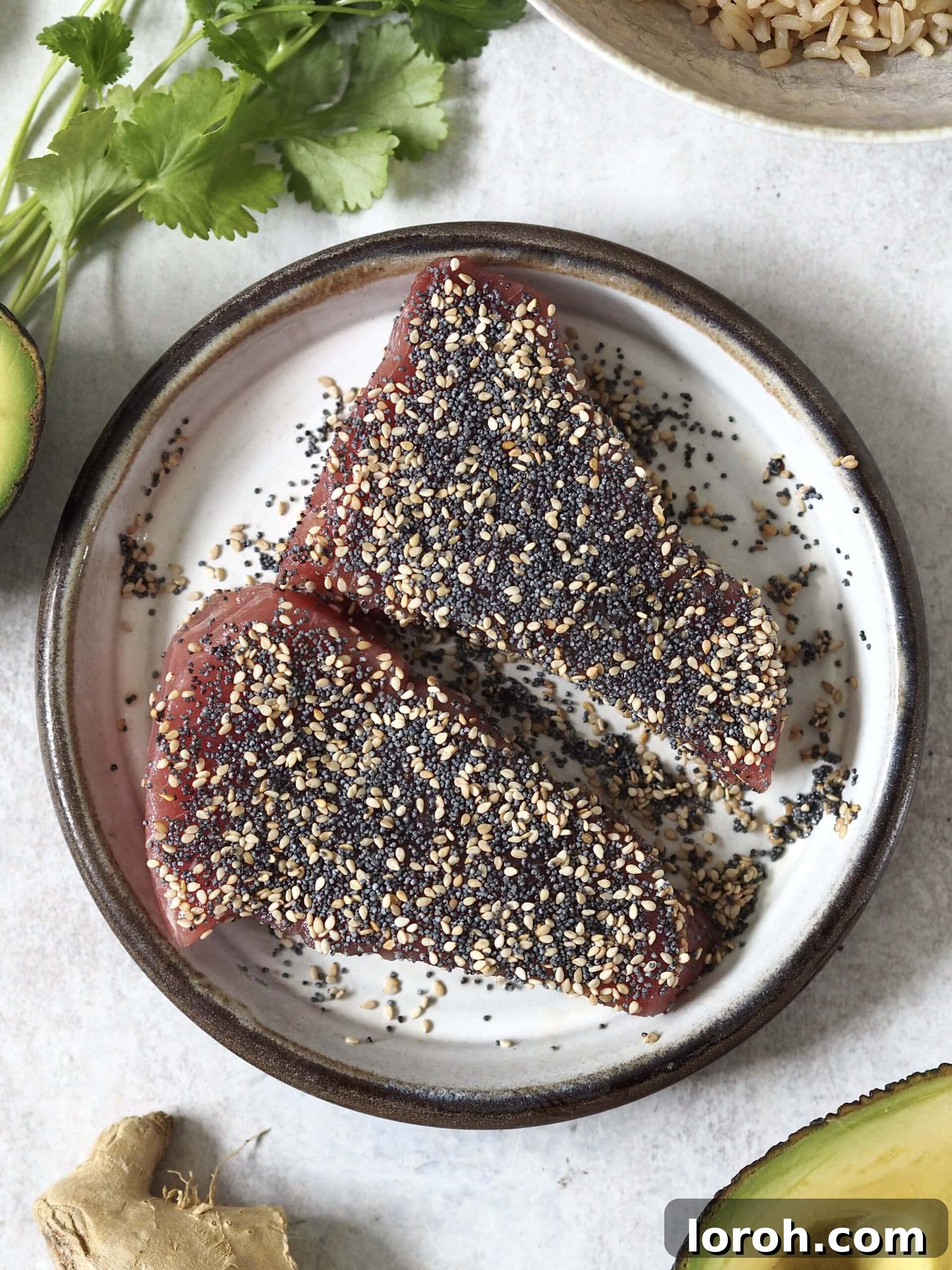 Two raw yellowfin tuna steaks coated in black and white sesame seeds, ready for searing.