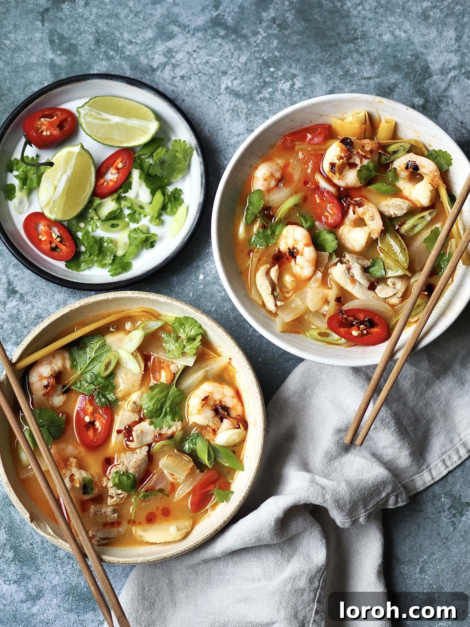 Vibrant Chicken and Prawn Tom Yum Soup 2 A vibrant bowl of chicken and prawn tom yum soup, garnished with fresh red chili slices and coriander leaves, set against a rustic background.