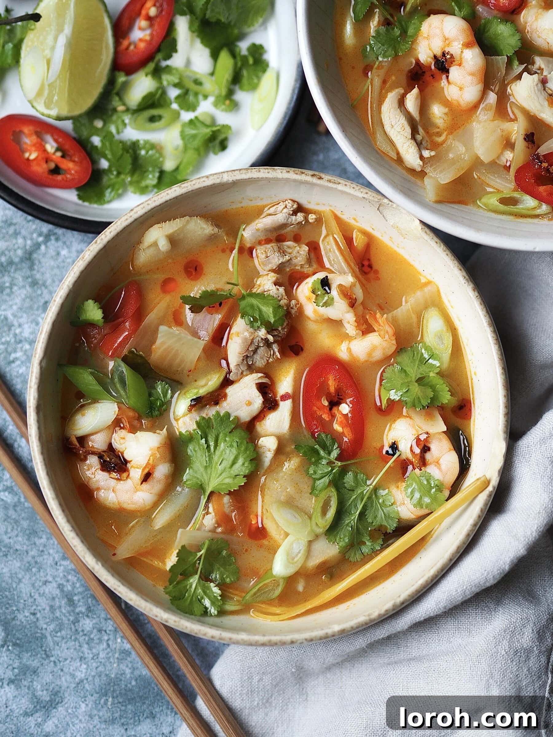 Vibrant Chicken and Prawn Tom Yum Soup 3 A close-up of the delicious chicken and prawn tom yum soup in a white bowl, garnished with a sprig of coriander and a slice of red chili.