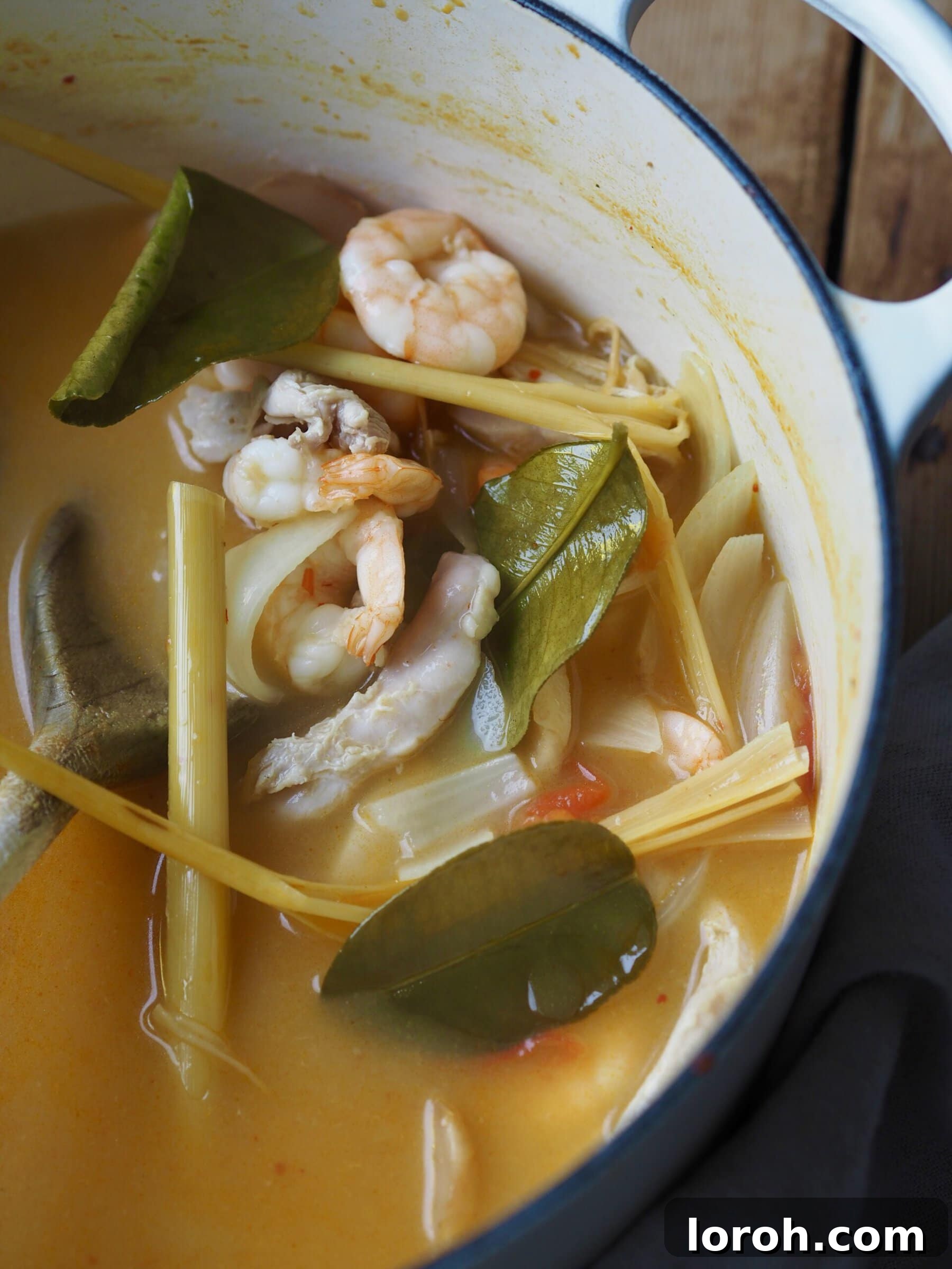Vibrant Chicken and Prawn Tom Yum Soup 8 Raw prawns and creamy coconut milk being stirred into the tom yum soup, alongside aromatics like lemongrass and ginger.