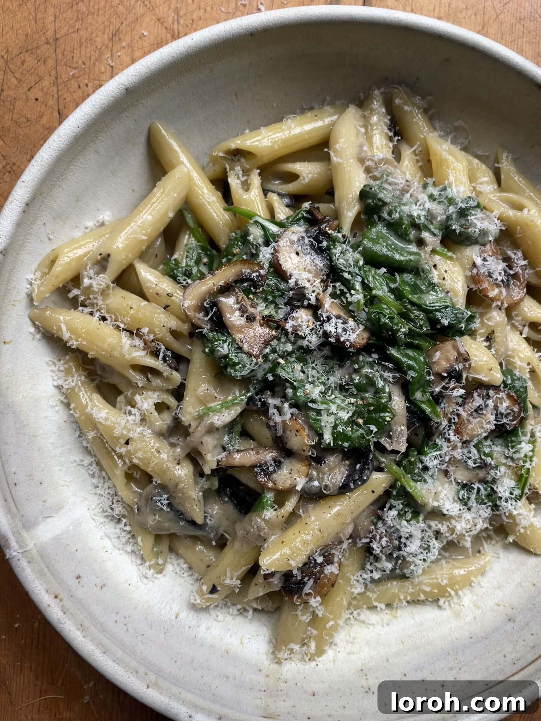 A close-up of creamy mushroom and spinach pasta, showcasing the rich sauce and perfectly cooked ingredients in a grey bowl.