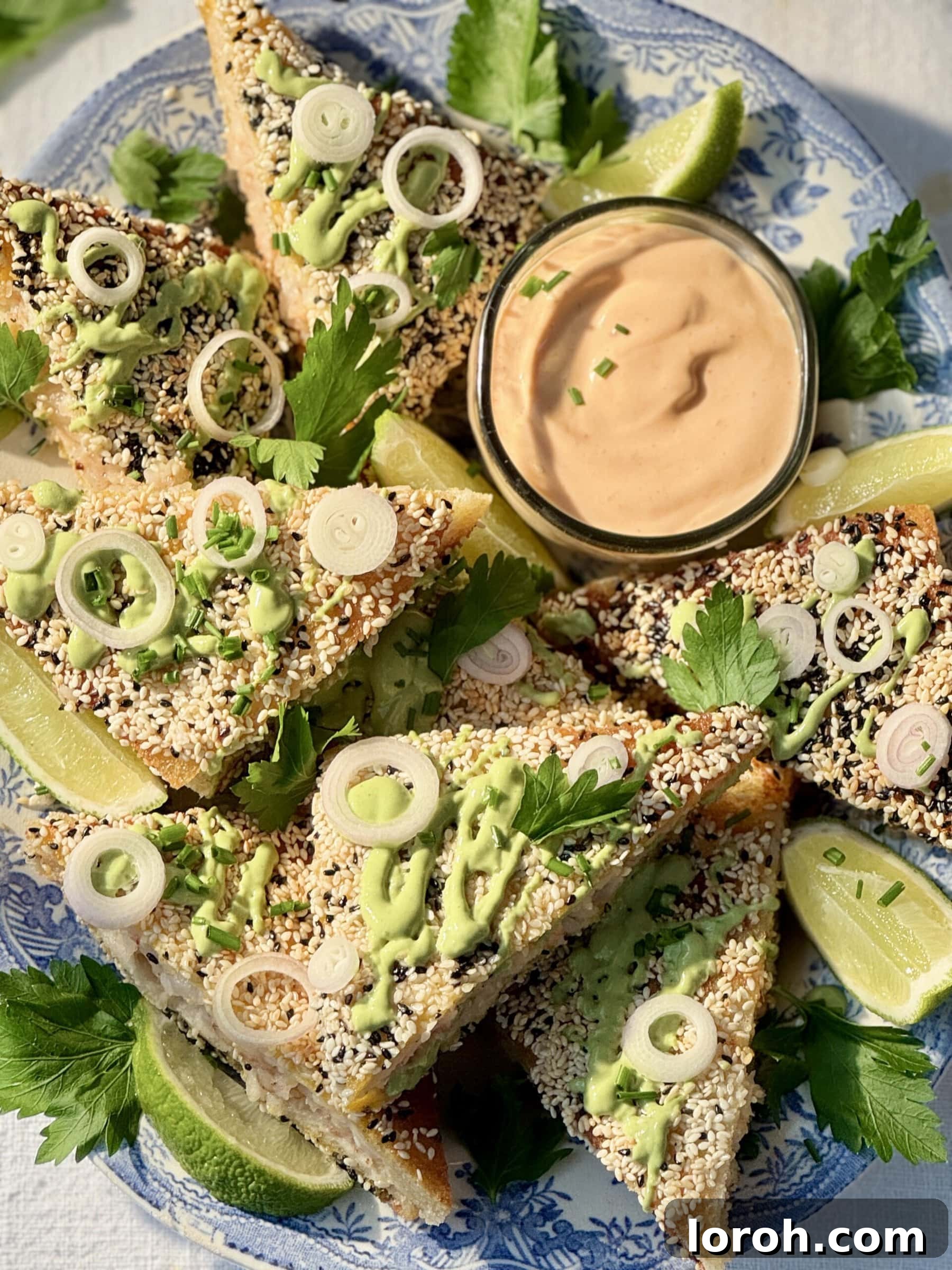 Golden Sesame Shrimp Crisps 12 Close-up of golden sesame prawn toasts drizzled with green sauce, accompanied by fresh lime wedges for serving.