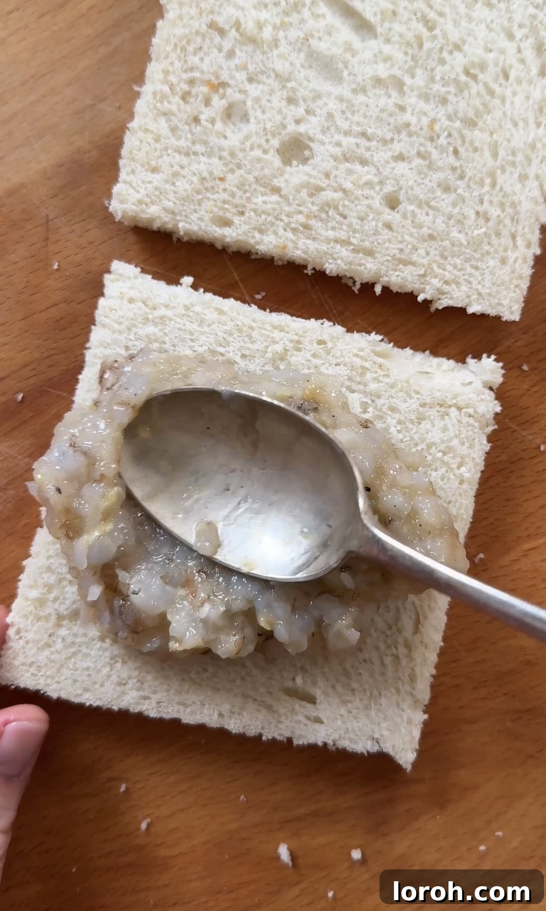 Golden Sesame Shrimp Crisps 8 Spreading the prawn mixture evenly onto one slice of crustless white bread, forming a sandwich.