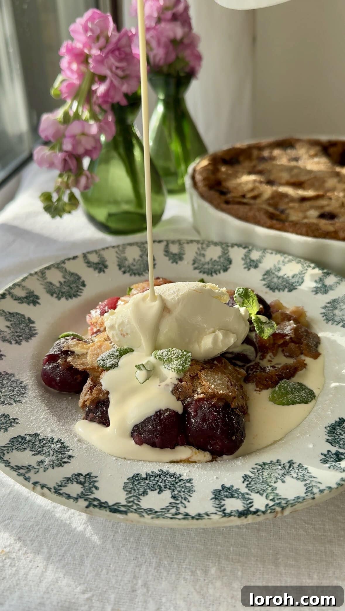 Classic French Cherry Clafoutis 2 Clafoutis aux Cerises in a bowl with cream being poured over the top, highlighting its rich, custardy texture.