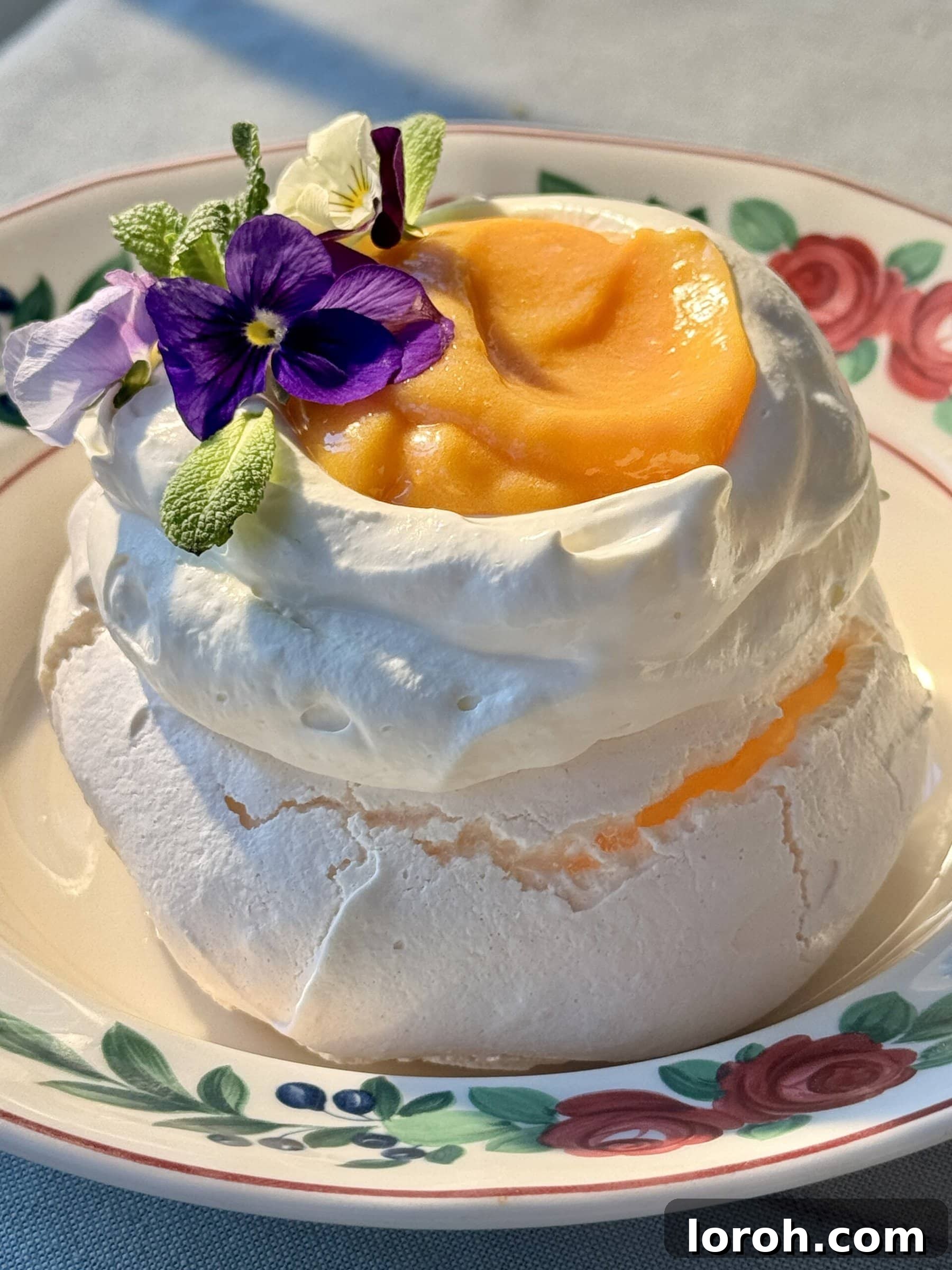 A single, perfectly formed lemon meringue on a pristine white plate, elegantly topped with whipped cream and a dollop of bright lemon curd.
