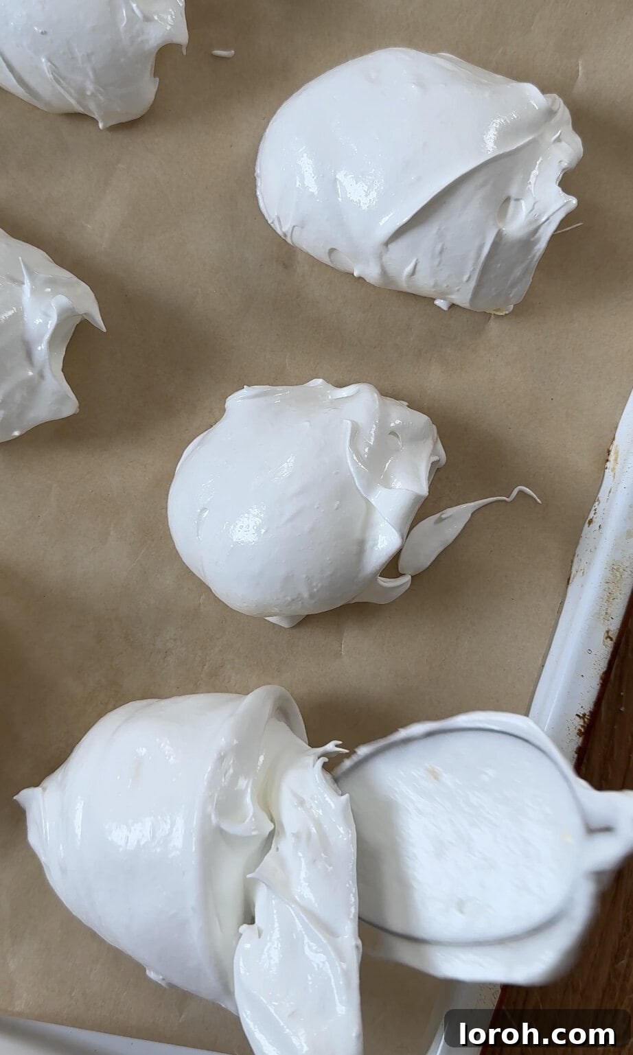 Scooping even mounds of lemon meringues onto a baking tray with two spoons, spaced apart.