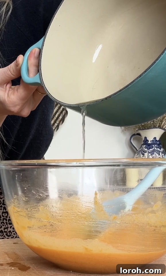 Gradually pouring hot lemon juice into the egg yolk mixture while whisking constantly and vigorously to temper the eggs.