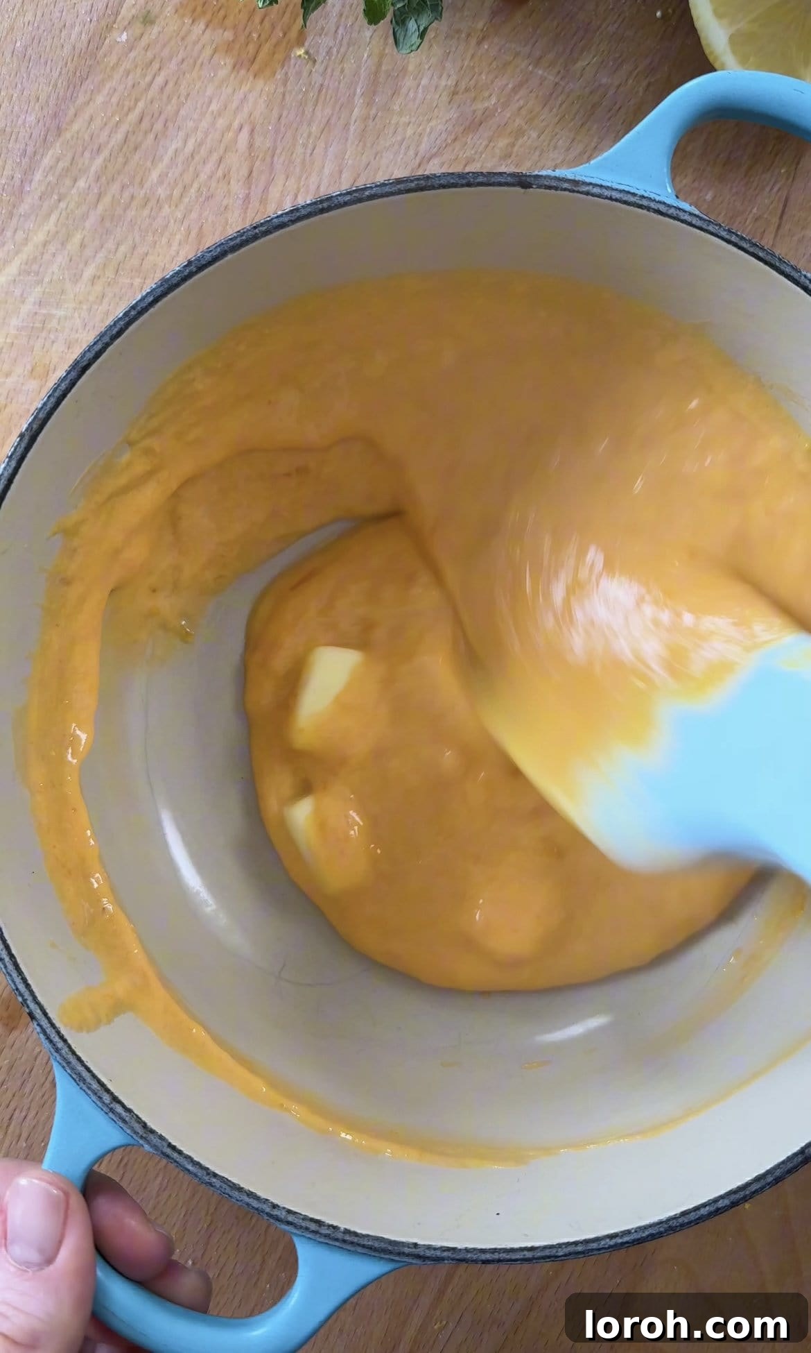 Adding diced unsalted butter to the hot, thickened lemon curd off the heat, stirring to melt and incorporate.