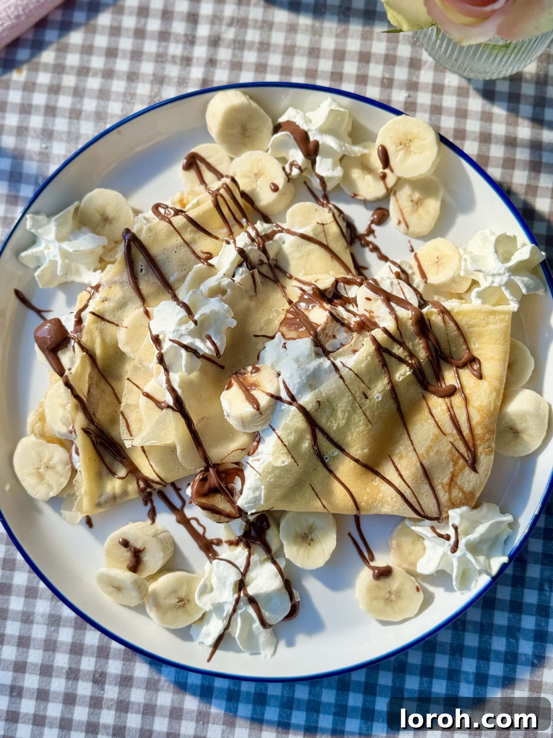 Golden Banana Crêpes 2 Delicious banana crepes artfully arranged on a plate, adorned with a swirl of whipped cream and a generous drizzle of melted Nutella, ready to be enjoyed.