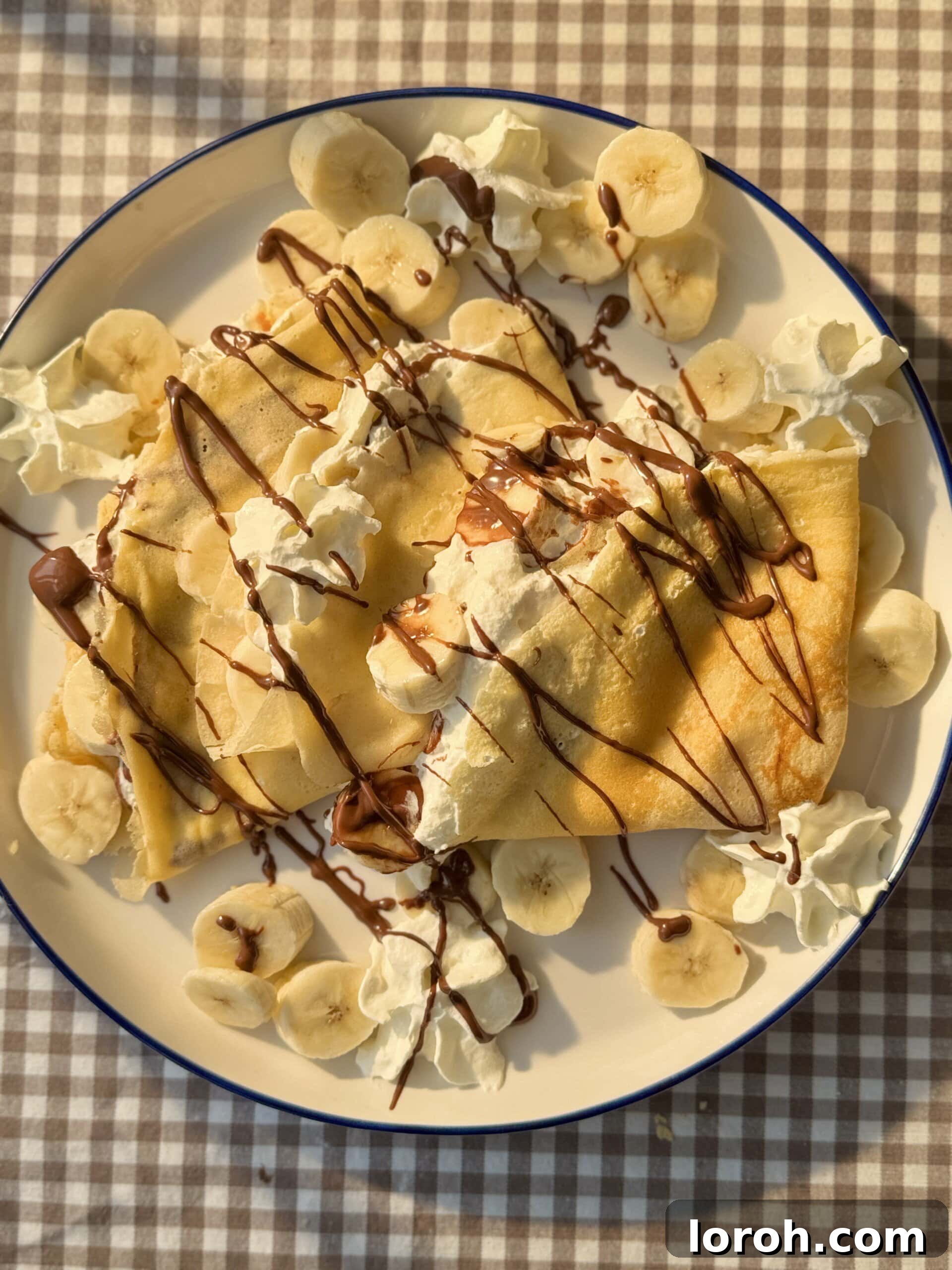 Golden Banana Crêpes 12 A vibrant display of banana crepes artfully arranged on a plate, generously topped with fluffy whipped cream and a luxurious drizzle of melted Nutella, a true feast for the eyes.