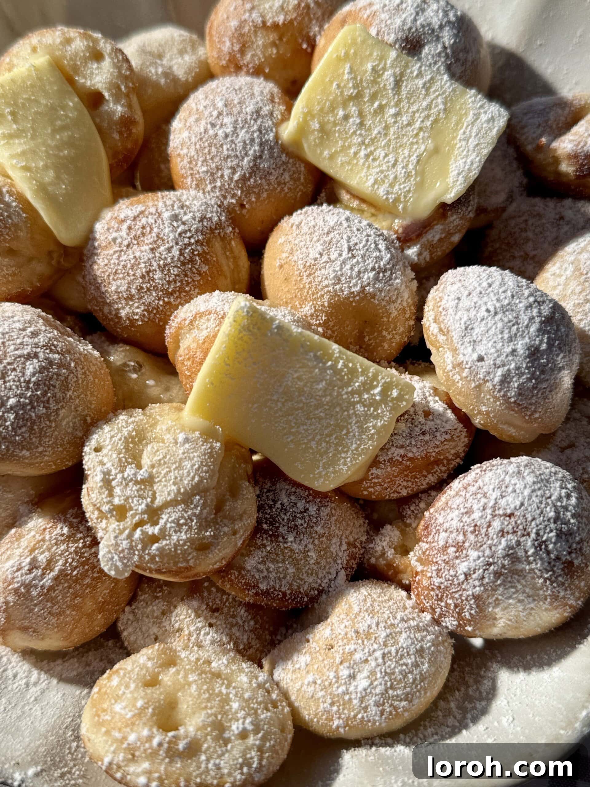 A bowl filled with warm poffertjes, topped with melting butter and a dusting of icing sugar.