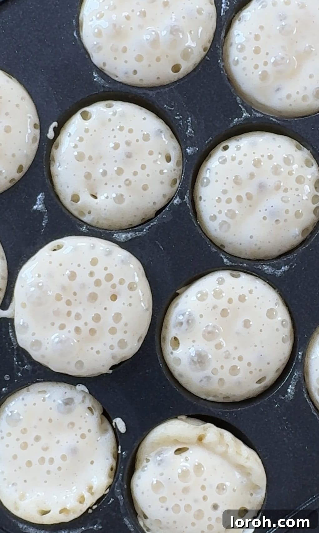 Close-up view of poffertjes frying in a specialized pan, showing the golden-brown edges.