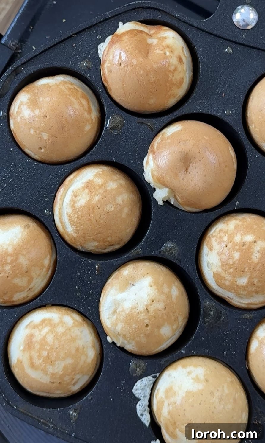 A hand using cocktail sticks to flip small poffertjes in a hot pan, demonstrating the cooking process.