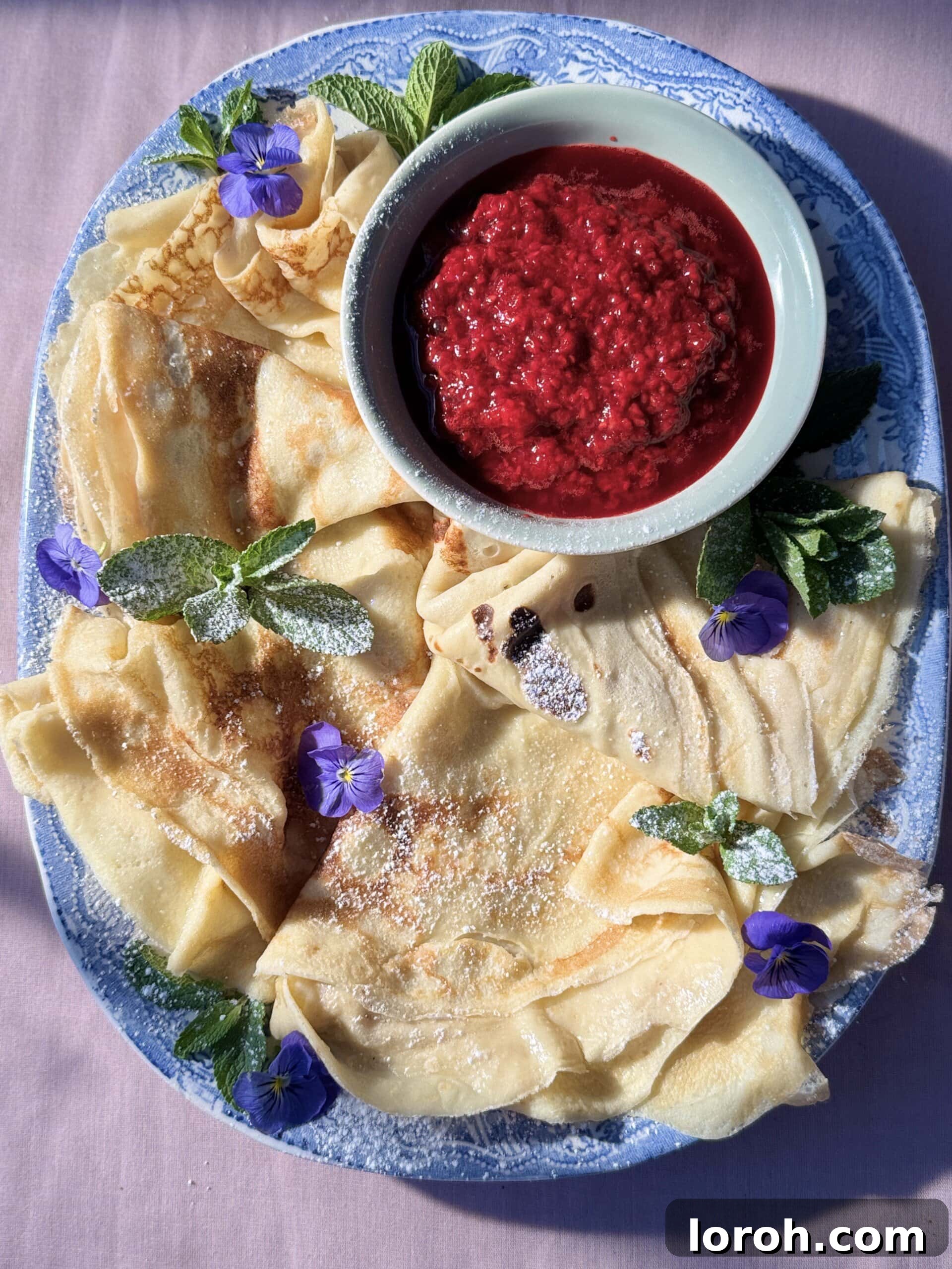 Three Pannekaker, folded into triangles, drizzled with raspberry compote and whipped cream.