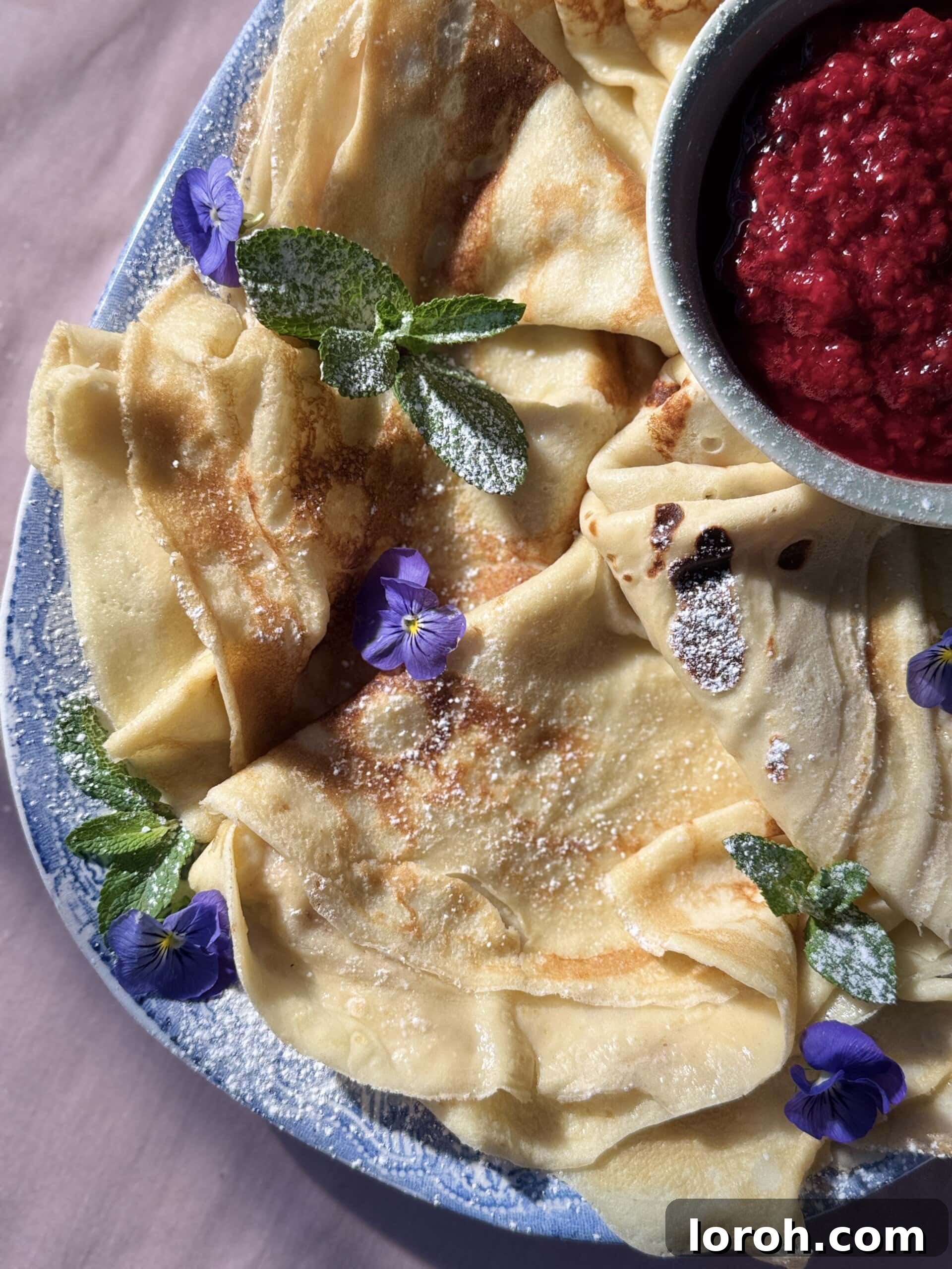 Close-up of freshly made Pannekaker, folded into quarters, stacked on a blue plate with raspberries and cream.