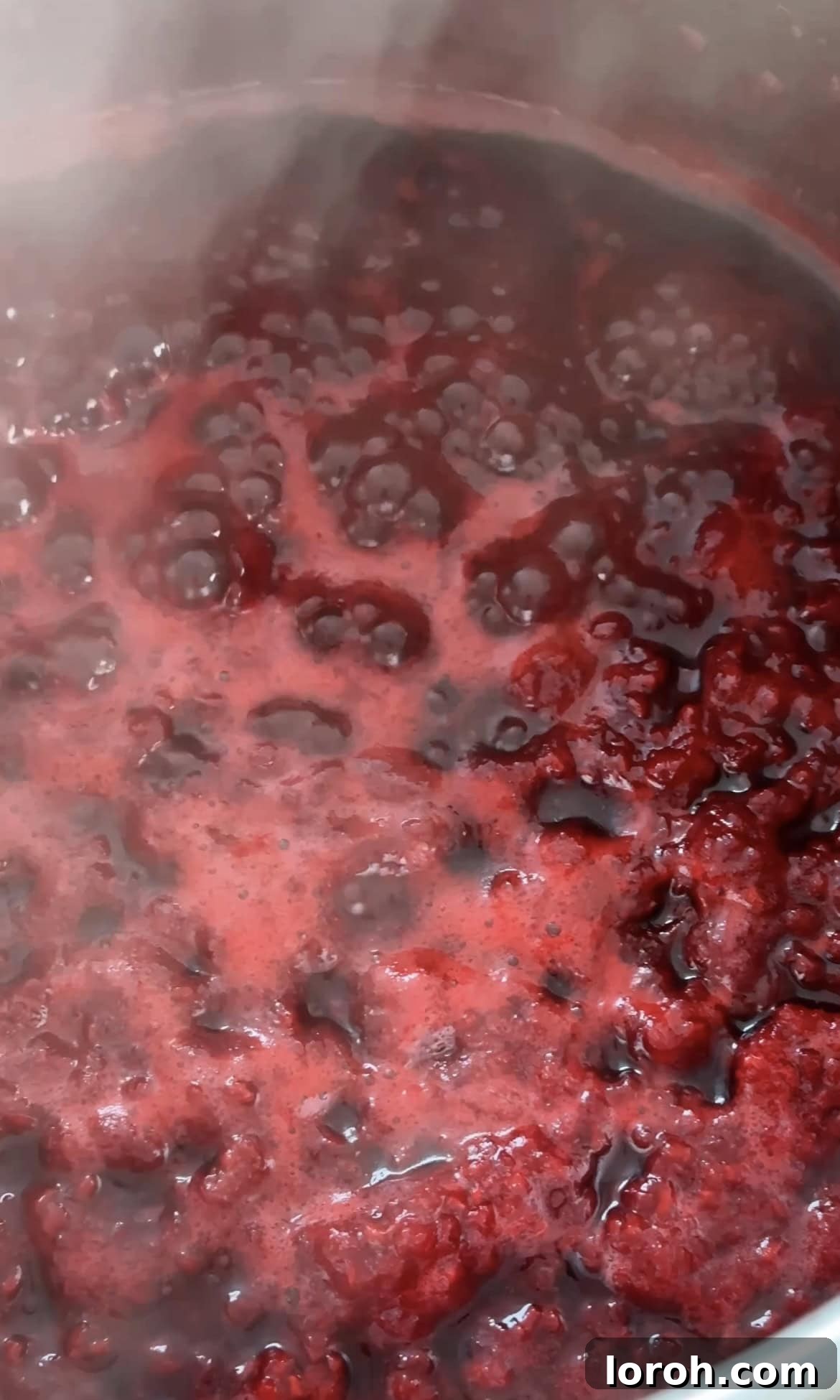 Raspberry compote gently bubbling in a saucepan, with raspberries softening.