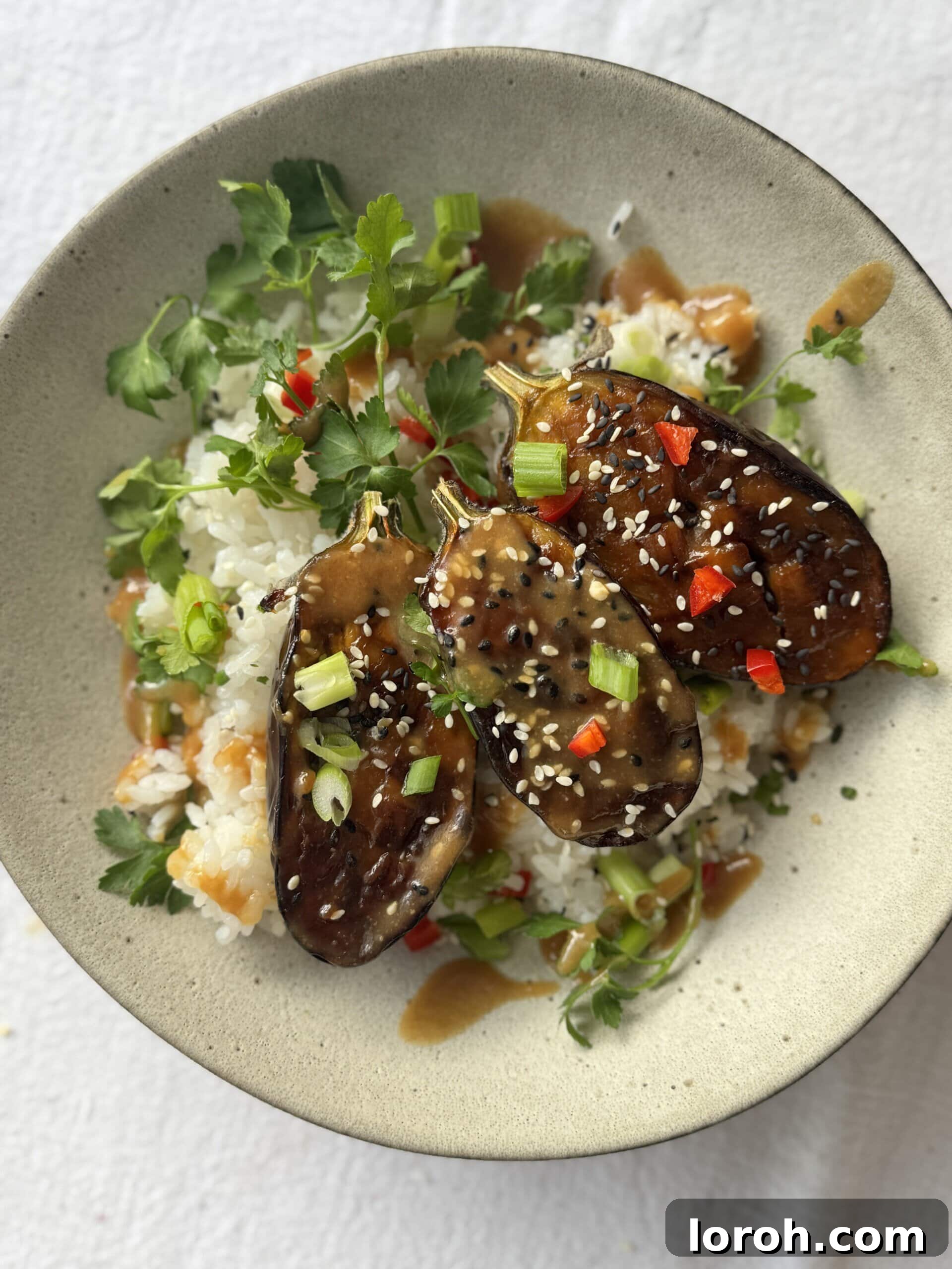 Miso aubergine in a bowl with rice, garnished with sesame seeds and chili.