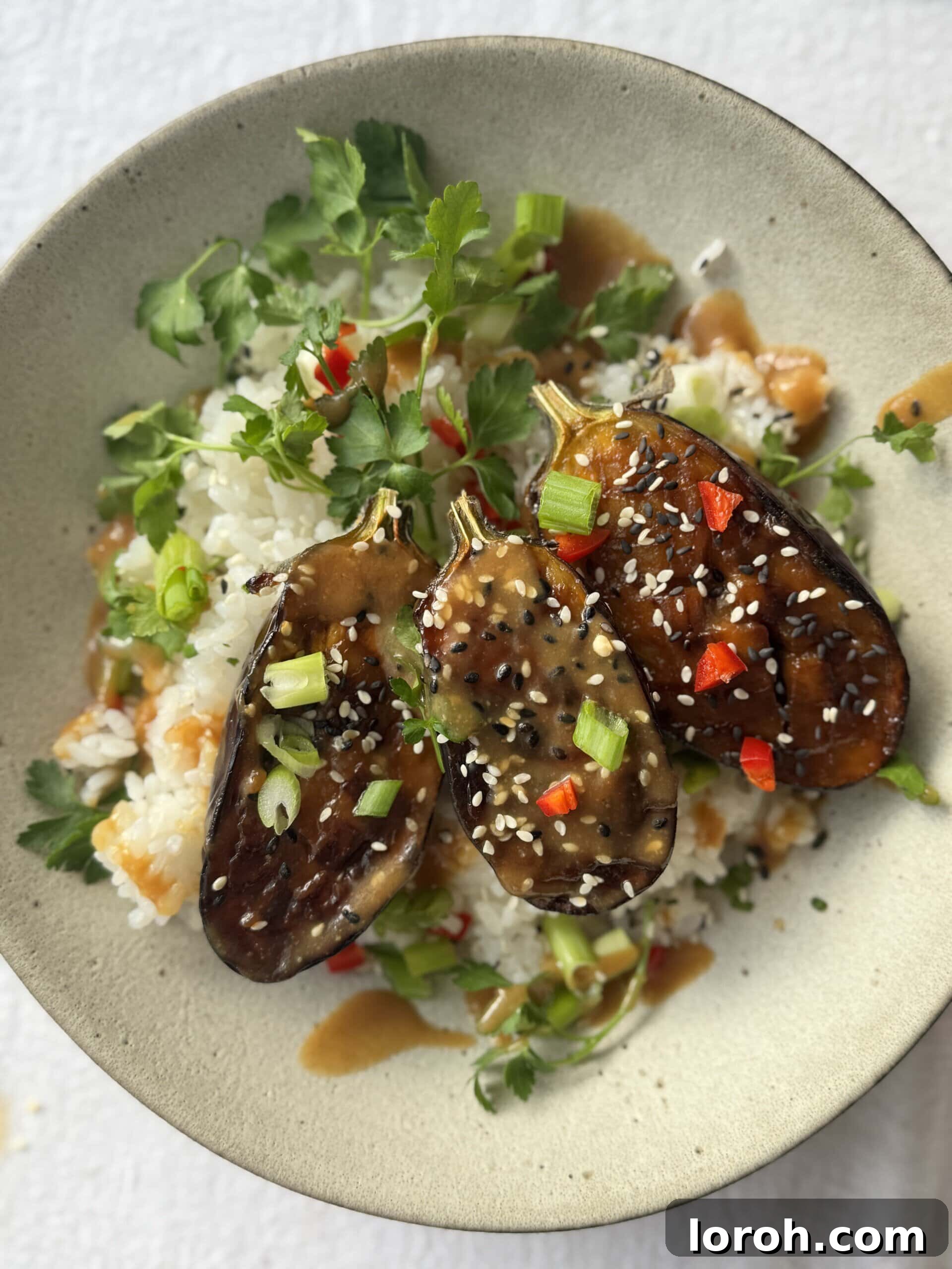 Miso aubergine served in a bowl with white rice, garnished with fresh herbs and chili.