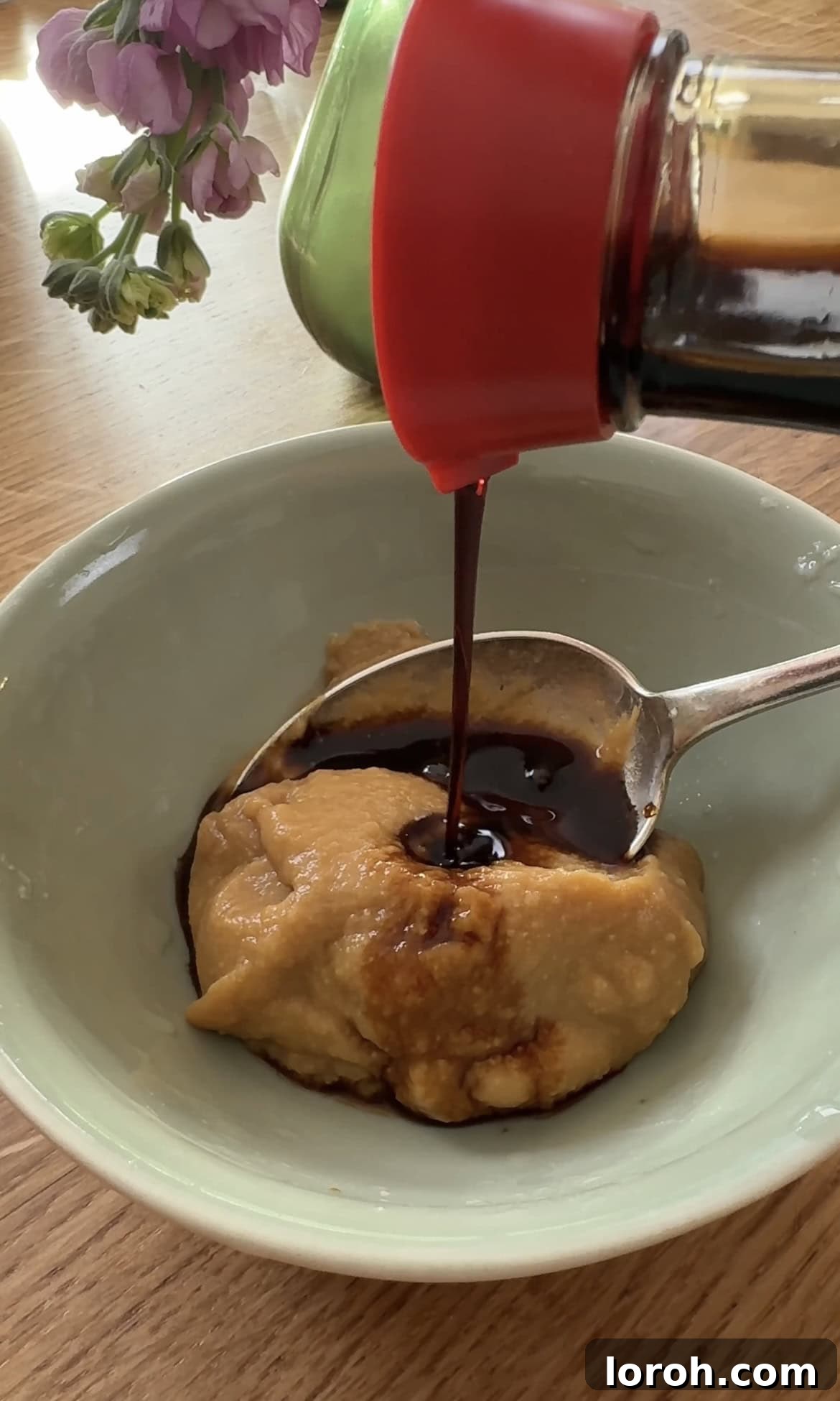 Adding soy sauce to miso paste in a bowl.