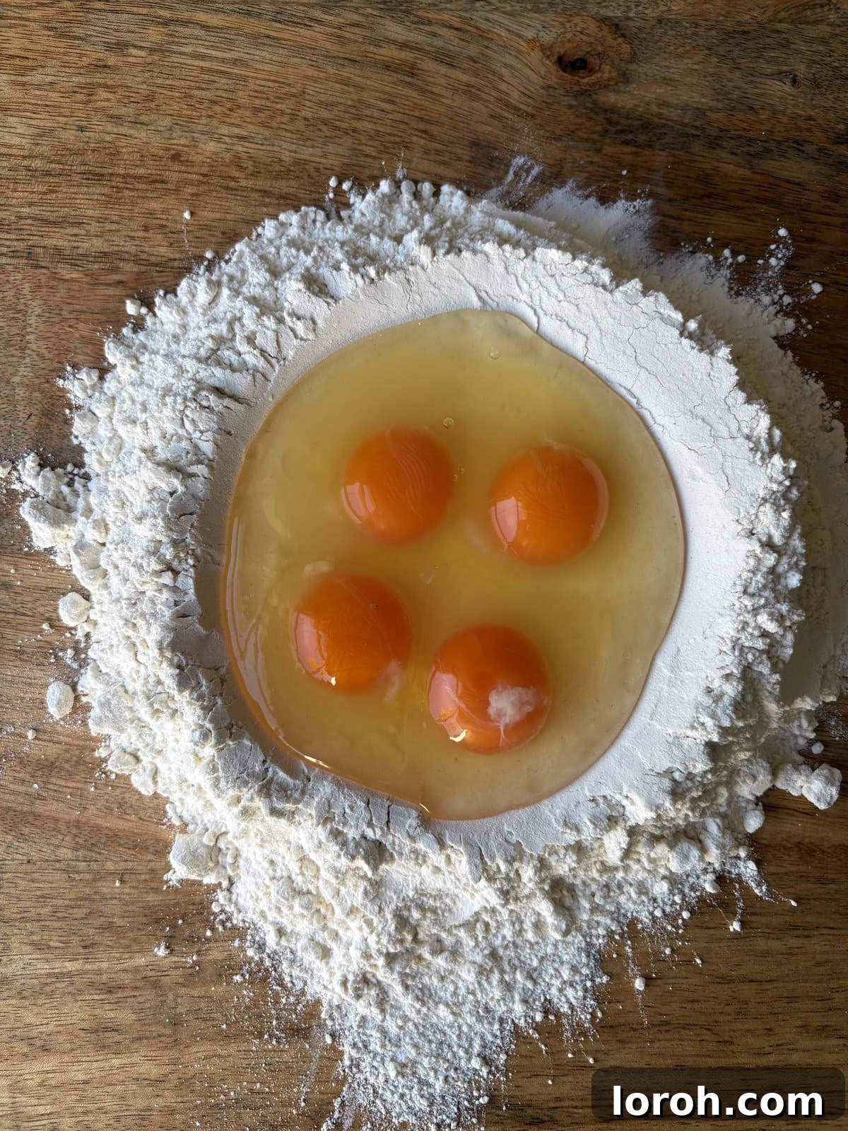 The Art of Homemade Pasta Dough 4 eggs cracked into a well of flour on a clean surface.