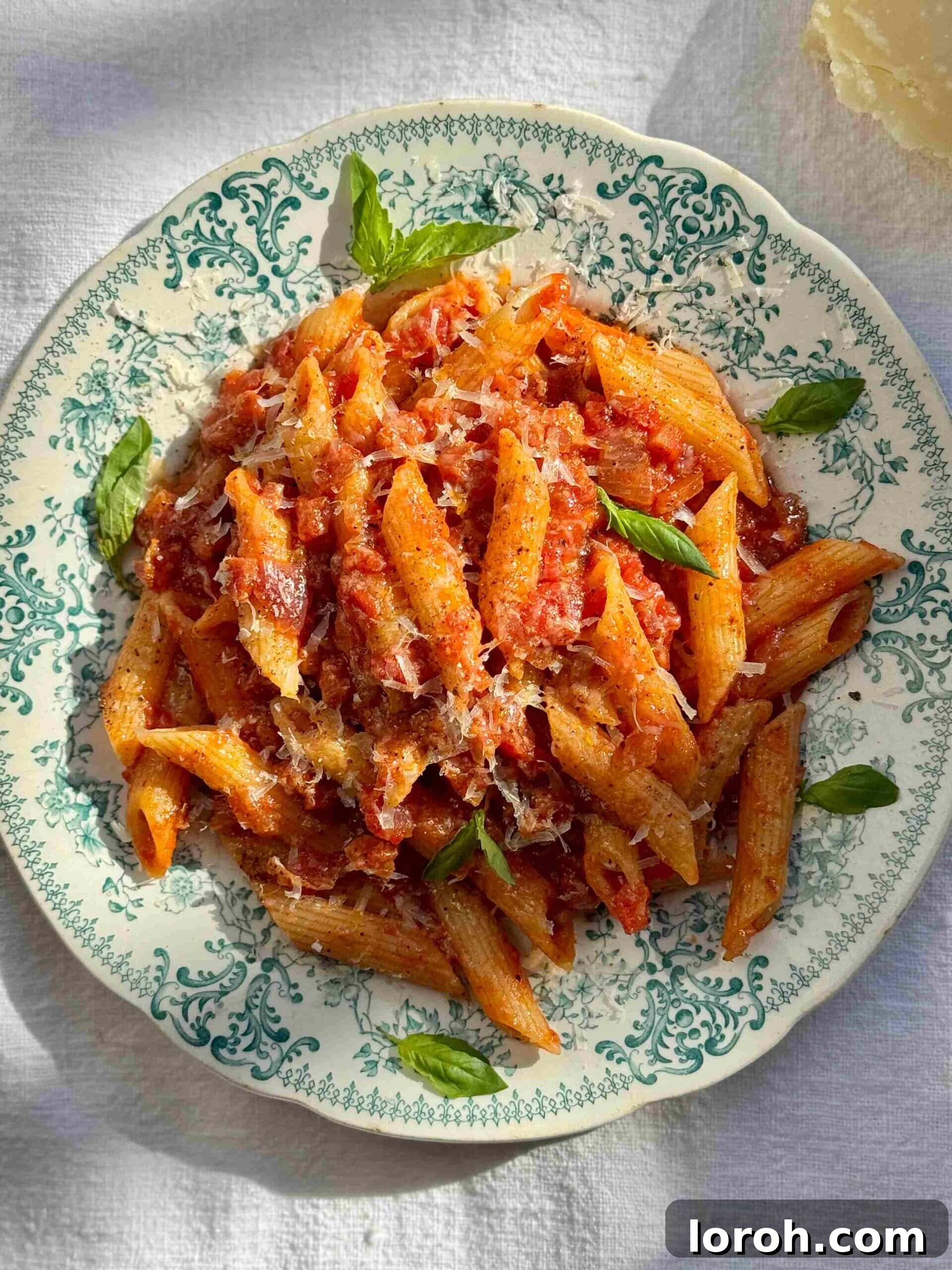 Guanciale Tomato Penne 4 A close-up shot of Penne Amatriciana served in a beautiful blue bowl, garnished with fresh herbs and grated cheese.