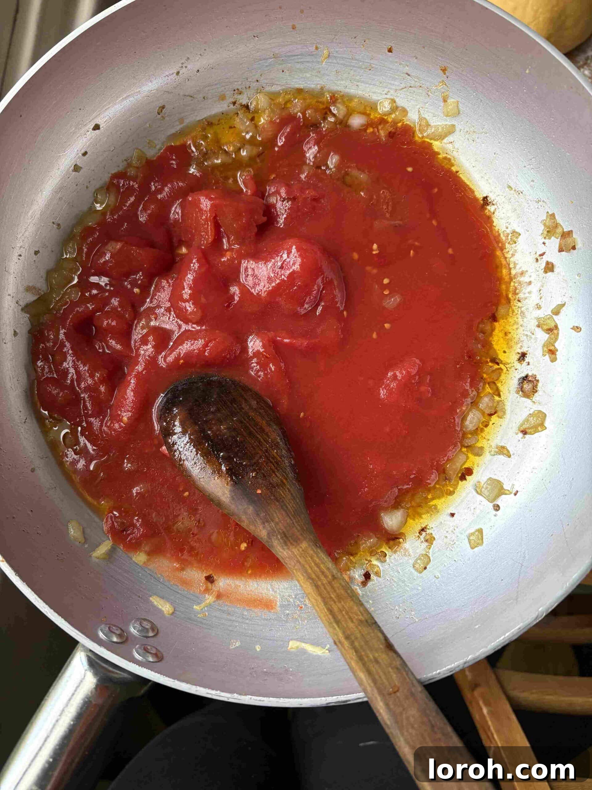 Guanciale Tomato Penne 7 Whole plum tomatoes being added to the sautéed onions and chili flakes in the frying pan, ready to simmer into a sauce.