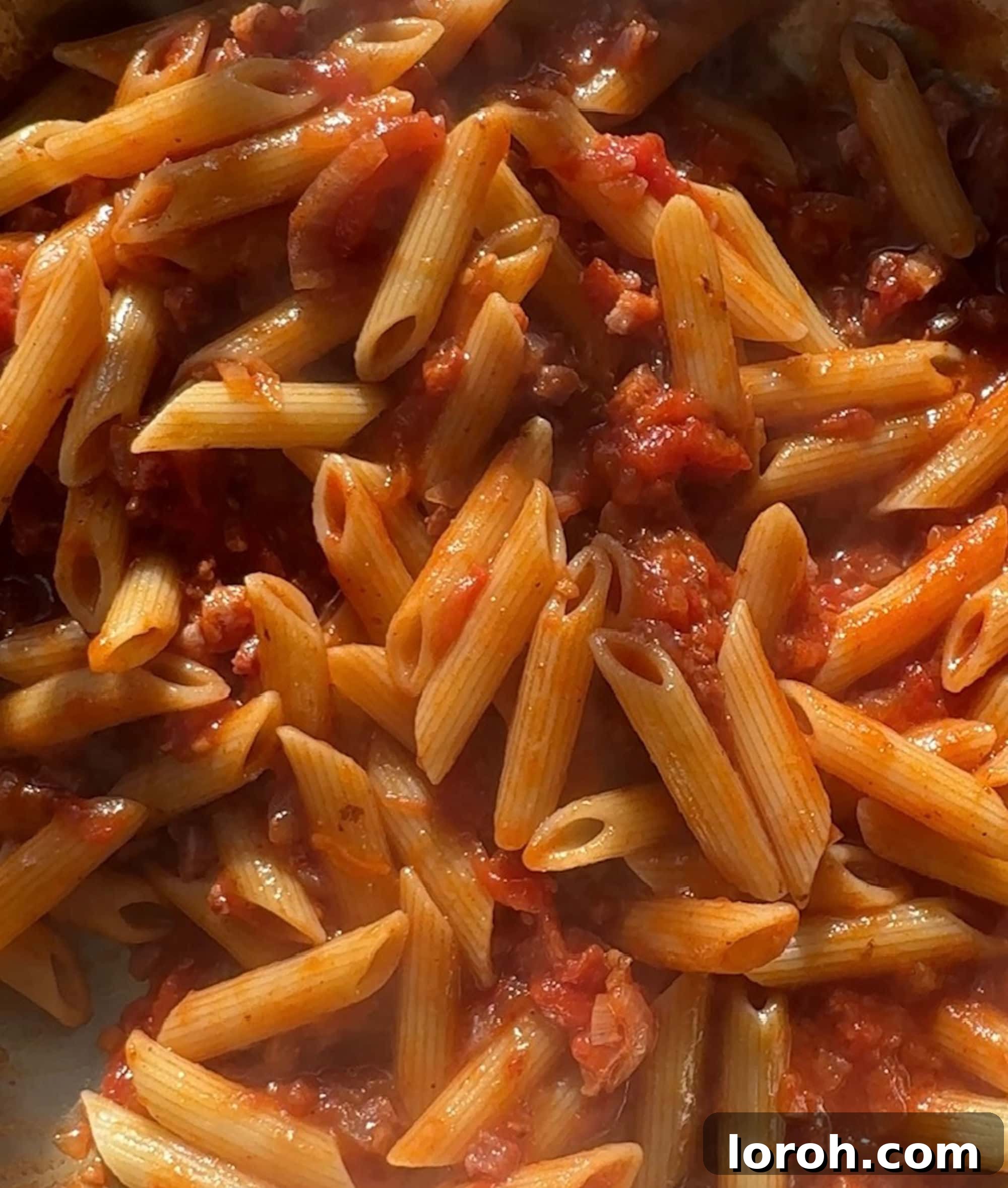 Guanciale Tomato Penne 10 Cooked penne pasta being tossed with the homemade Amatriciana sauce in a large pan, coating each piece evenly.